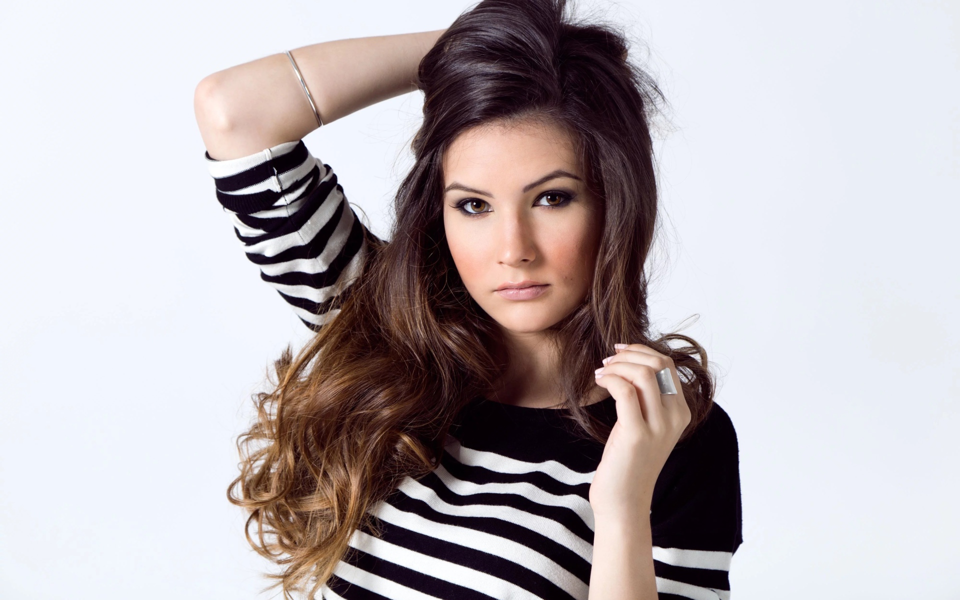 Девушка в полосатом свитере с рукой в волосах на белом фоне