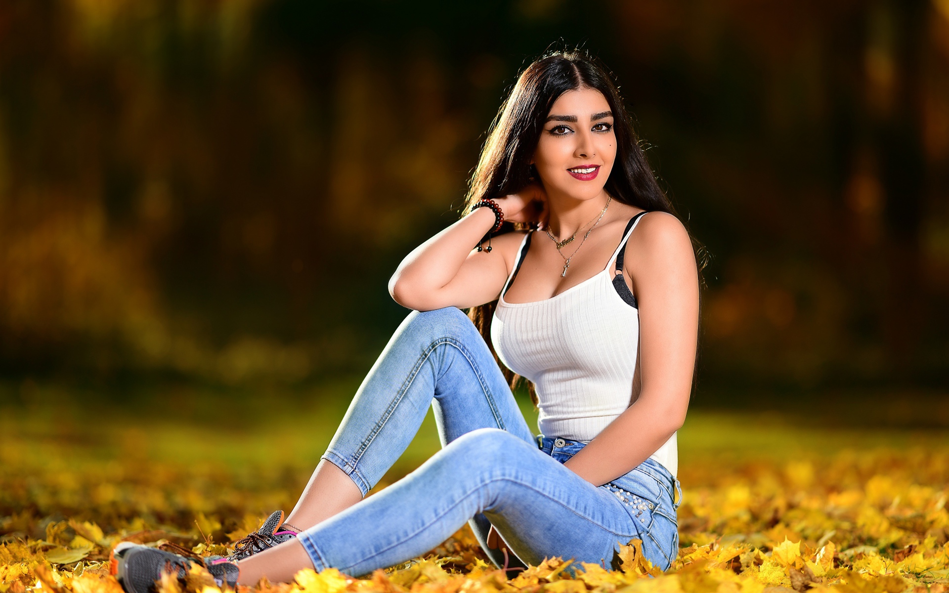 Улыбающаяся брюнетка сидит на опавшей листве