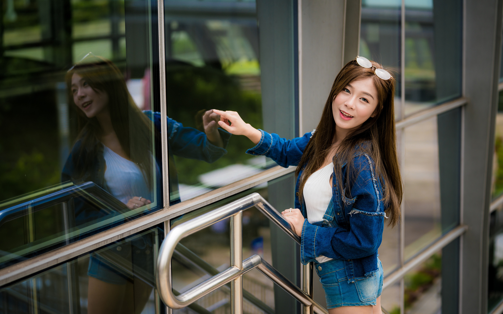 Улыбающаяся девушка в джинсовой куртке стоит у стены 