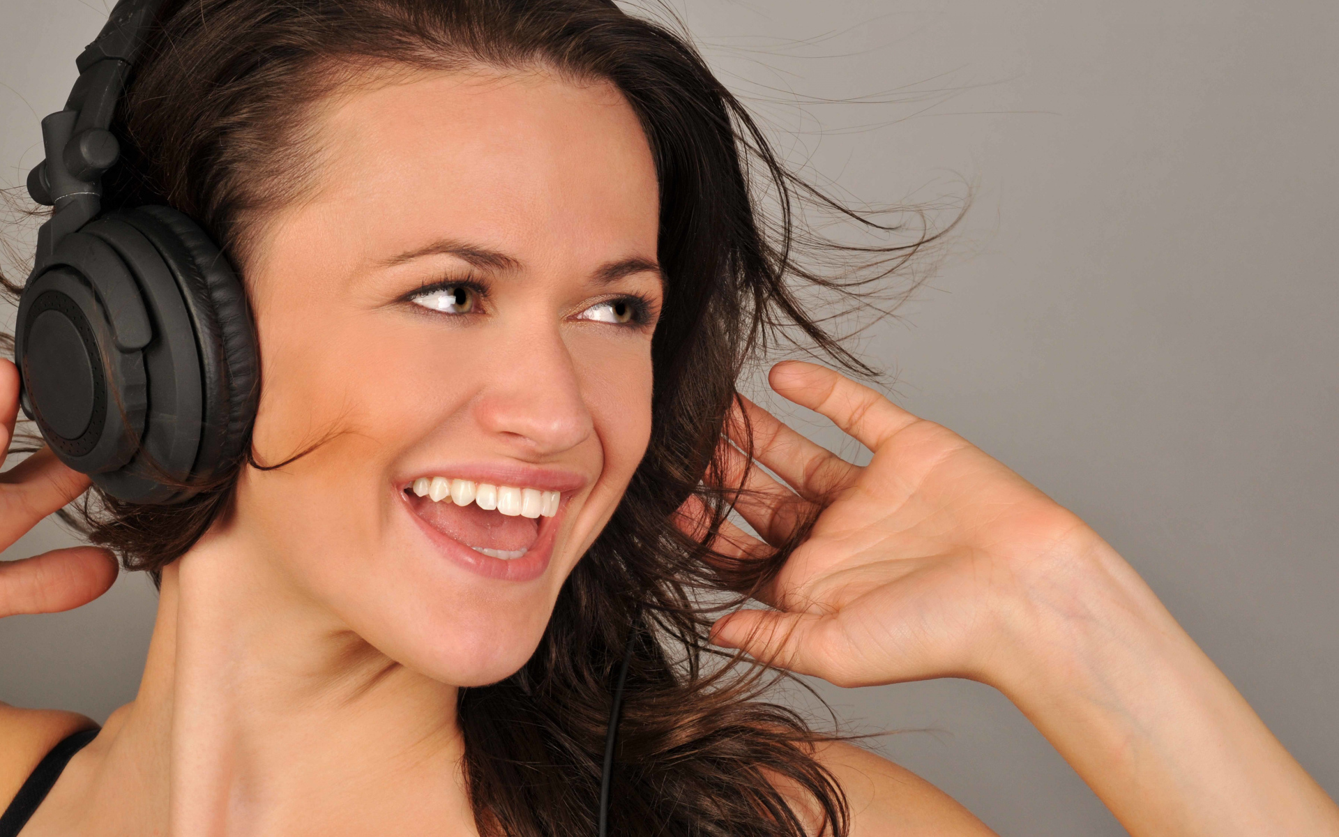 Улыбающаяся девушка в наушниках на сером фоне 