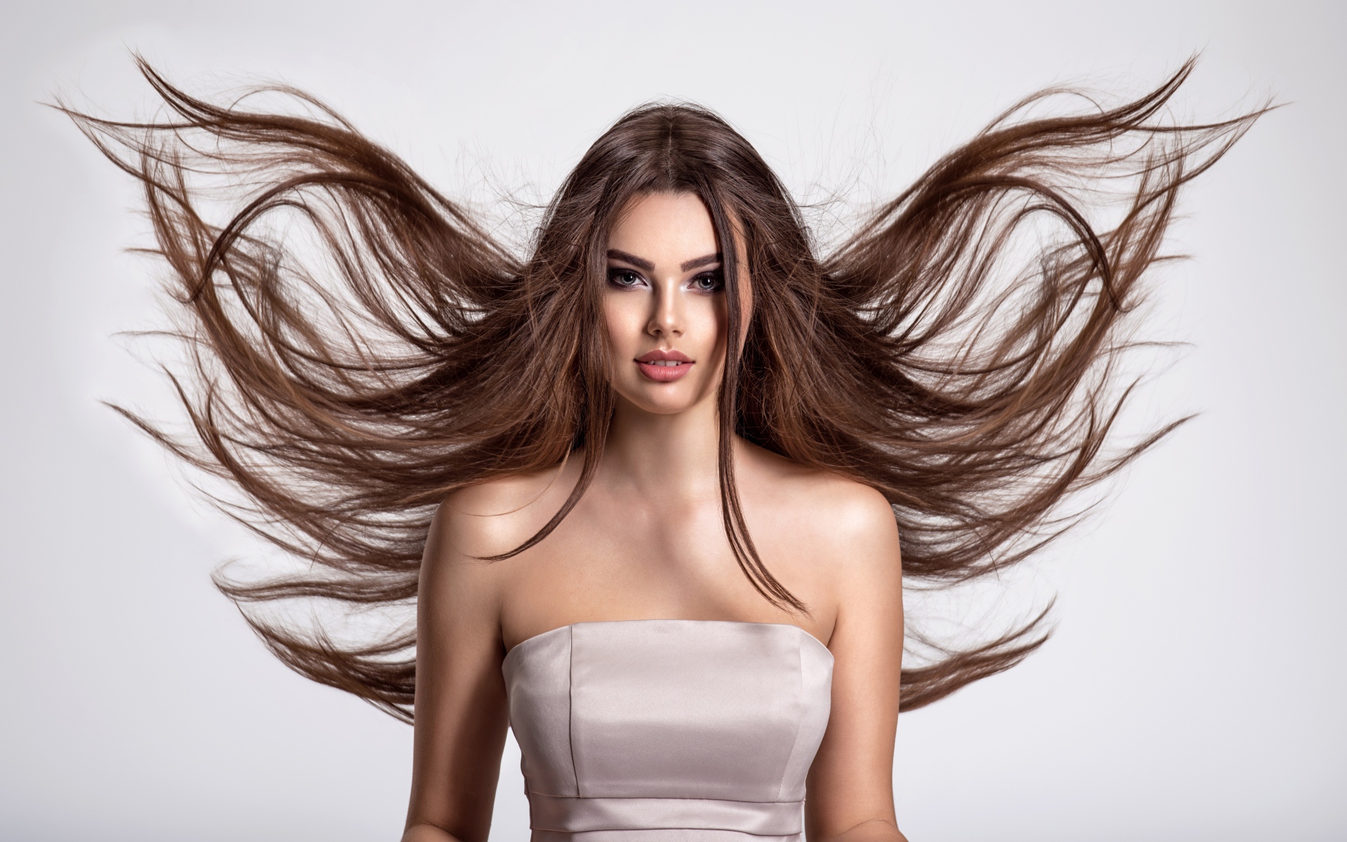 Ветер развивает волосы красивой девушке шатенке на сером фоне