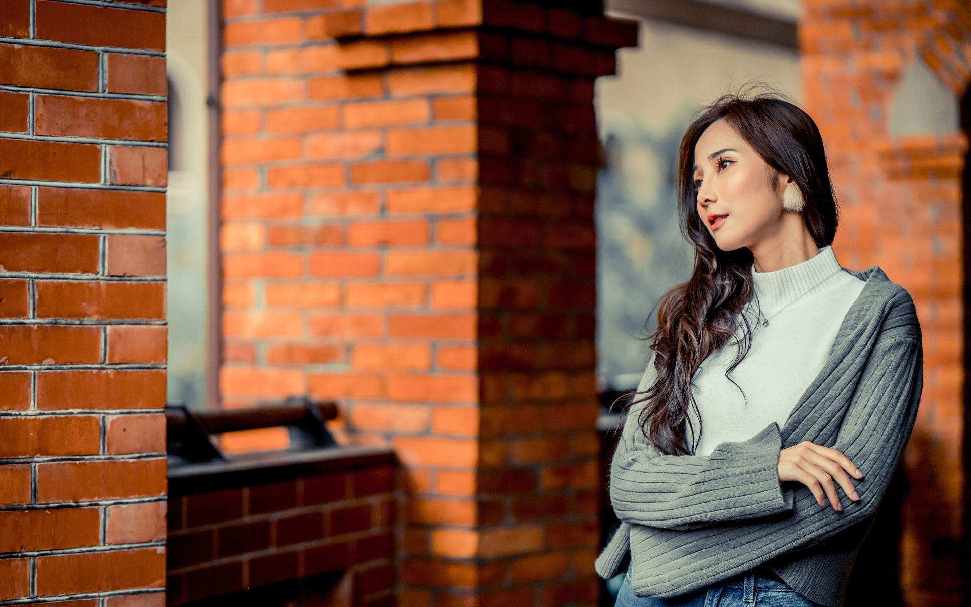 Молодая девушка азиатка в серой кофте у кирпичной стены 