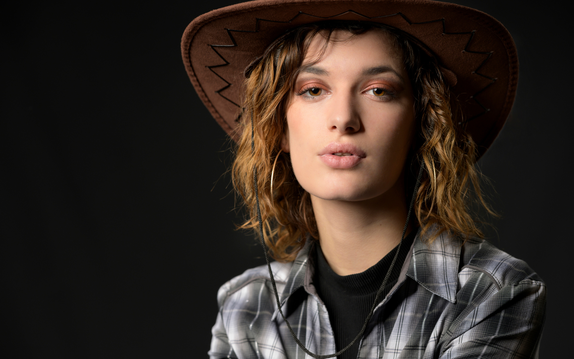 Молодая девушка в ковбойской шляпе на сером фоне
