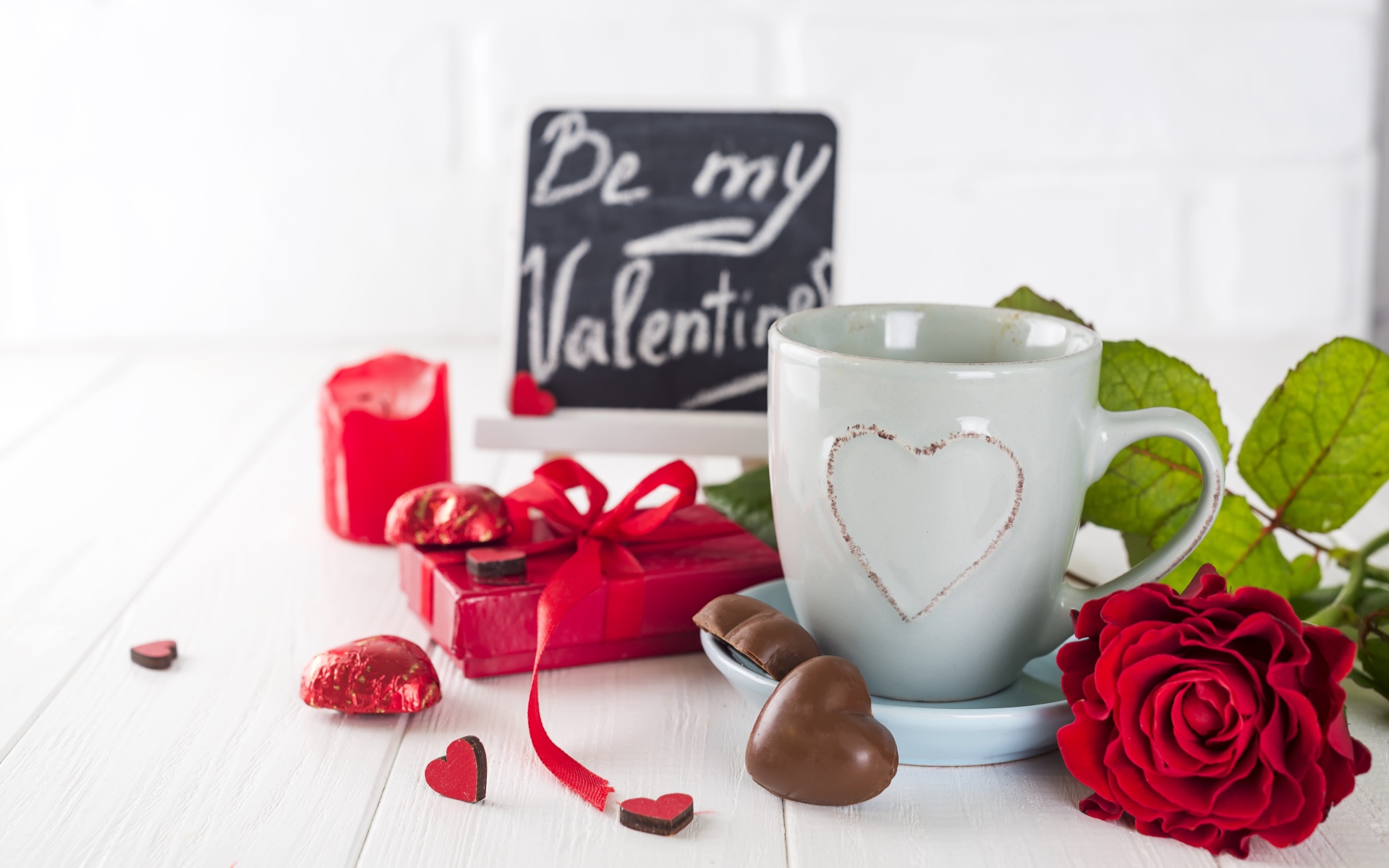 Белая чашка с конфетами и красной розой на столе в подарок на 14 февраля