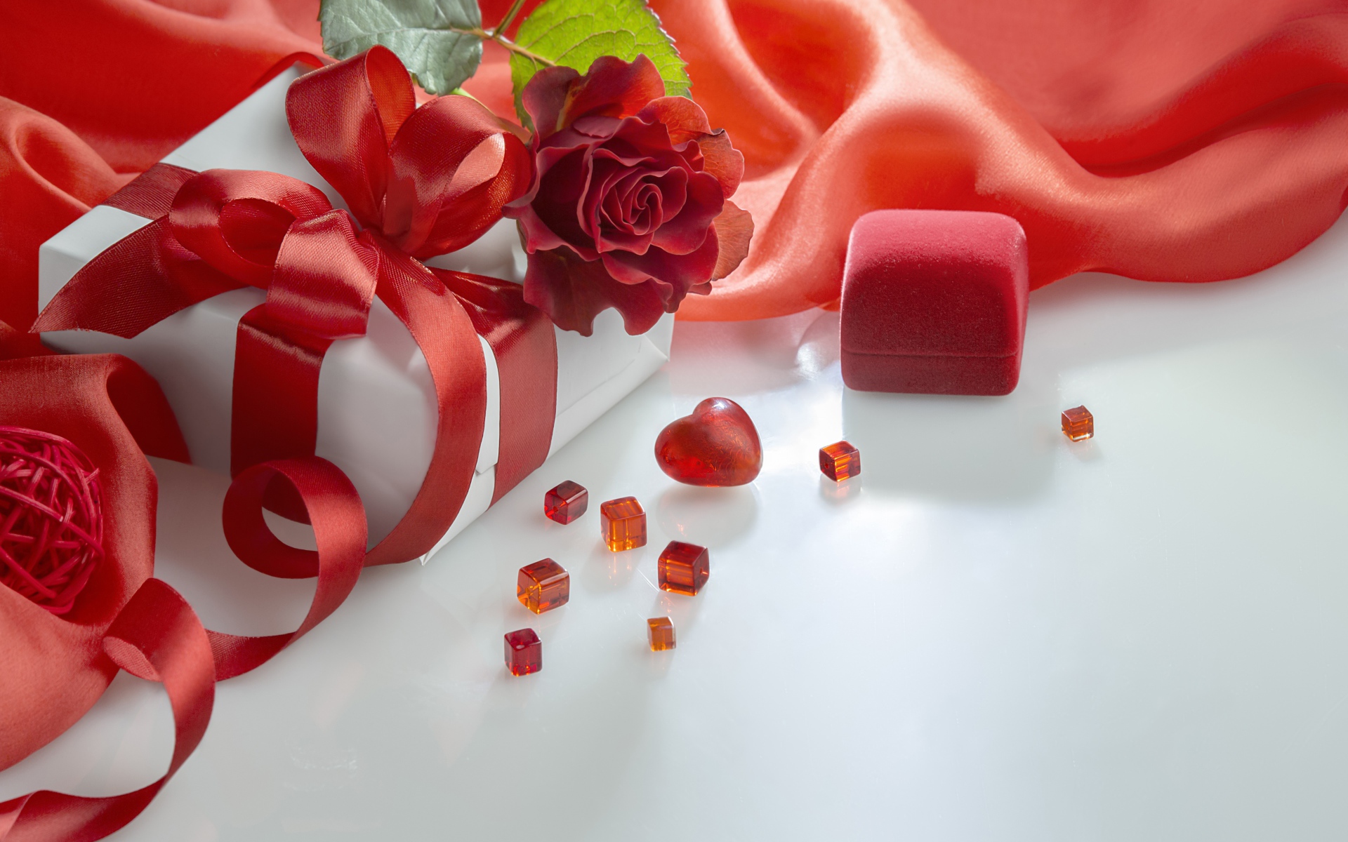 Подарки на белом столе с розой и красной тканью