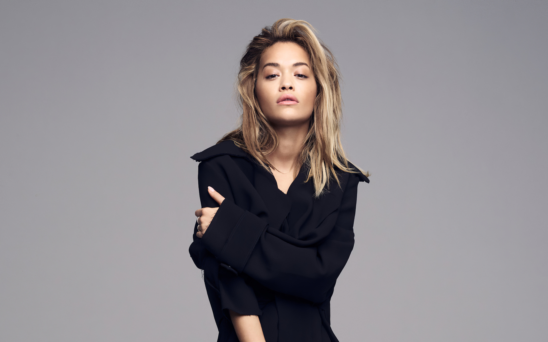 Певица Рита Ора в черном наряде на сером фоне