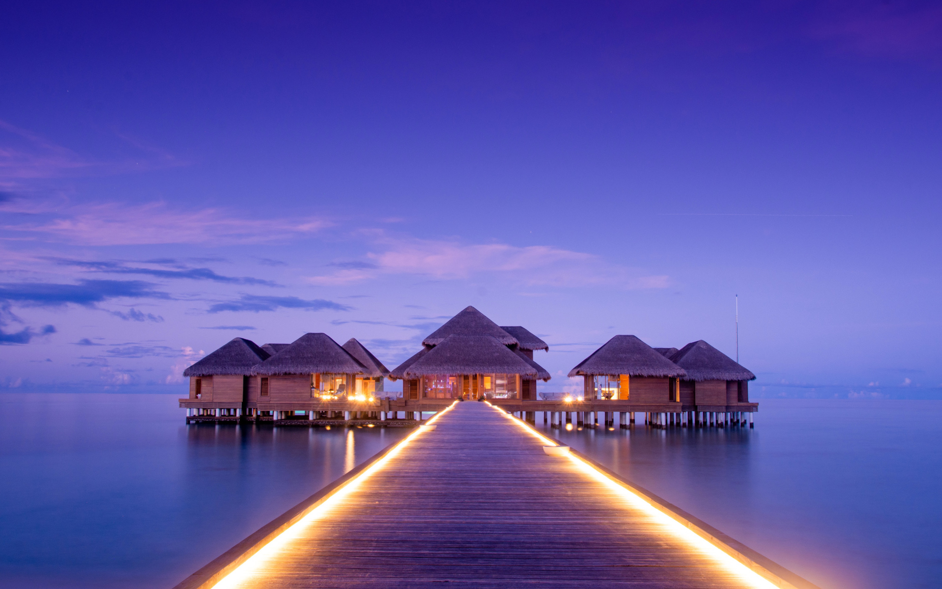 Мост с подсветкой идет к домам на сваях в океане