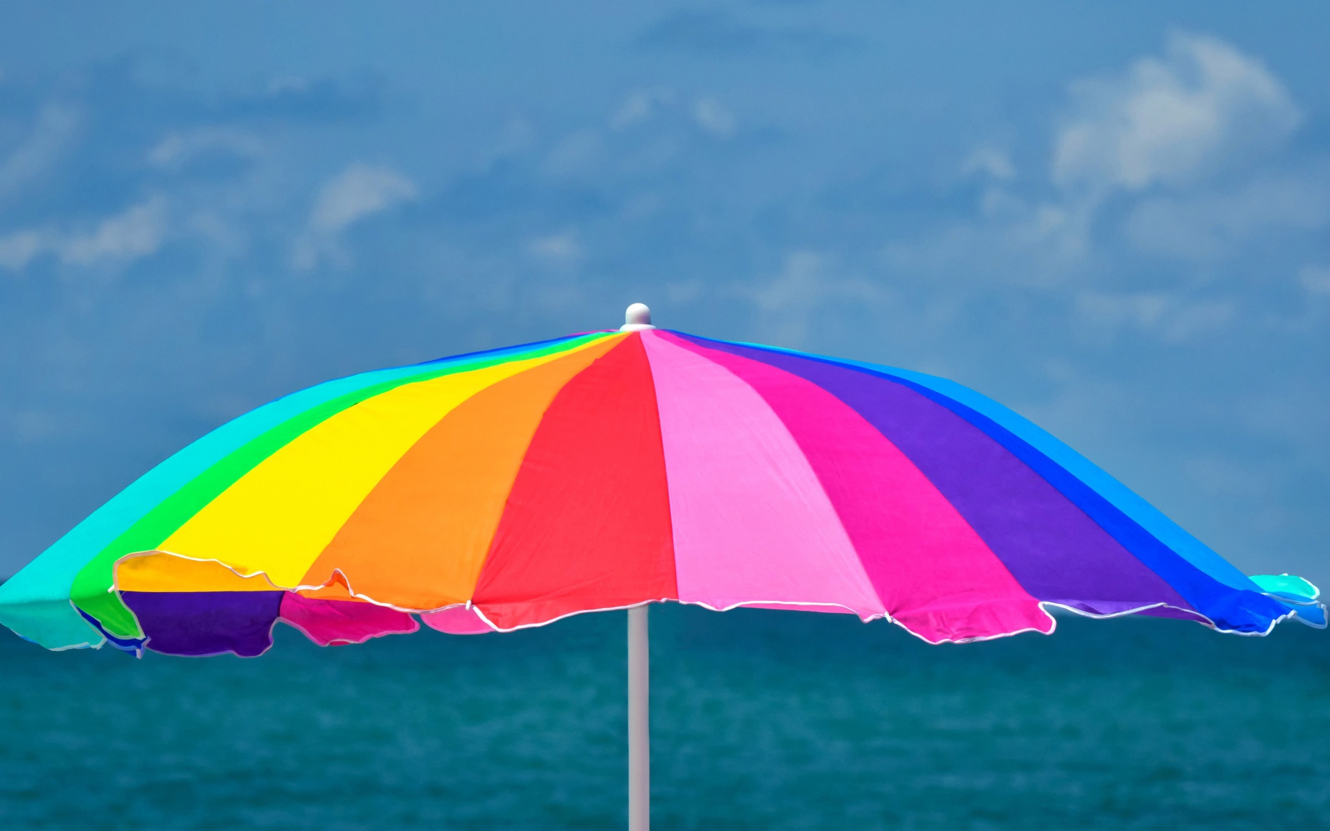 Большой разноцветный пляжный зонт на фоне моря