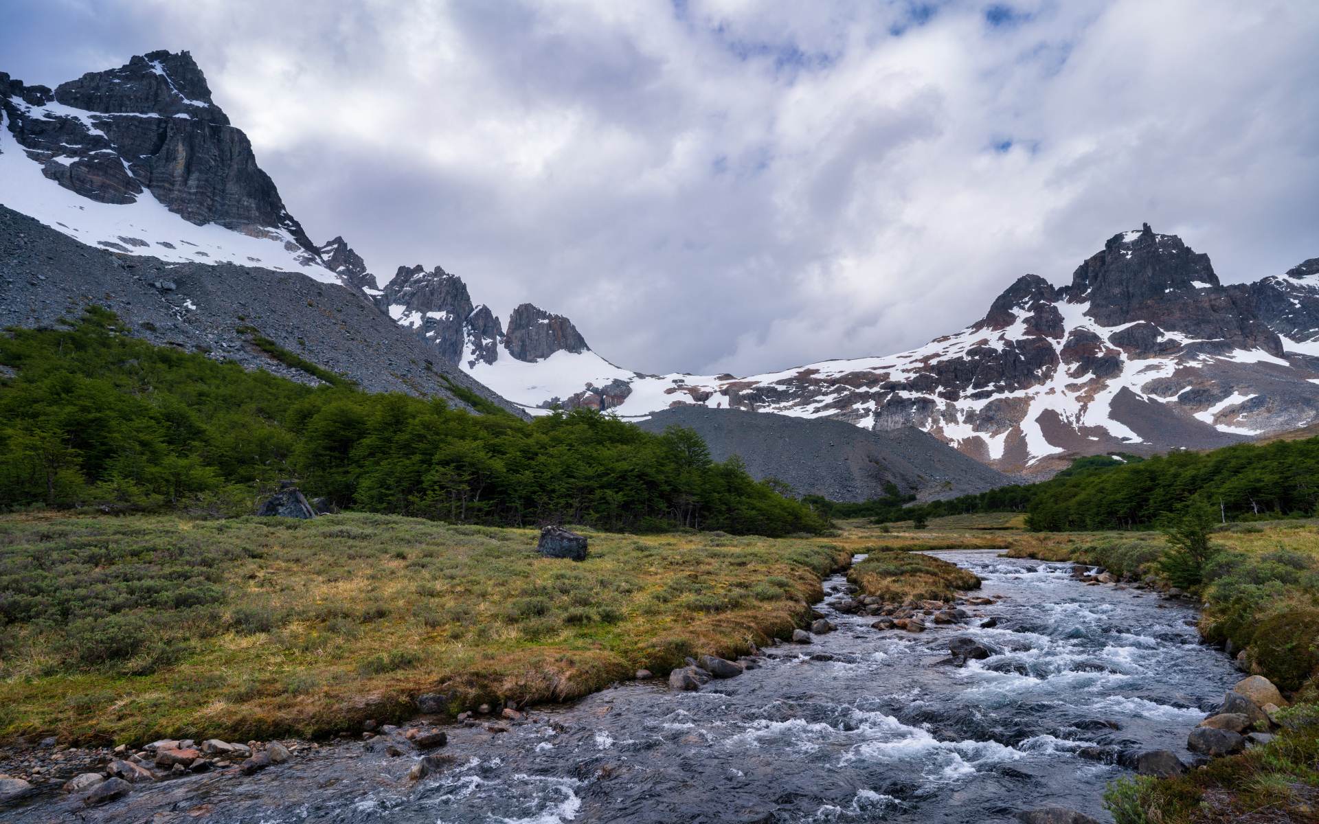 Быстрая река у заснеженных гор под густыми белыми облаками