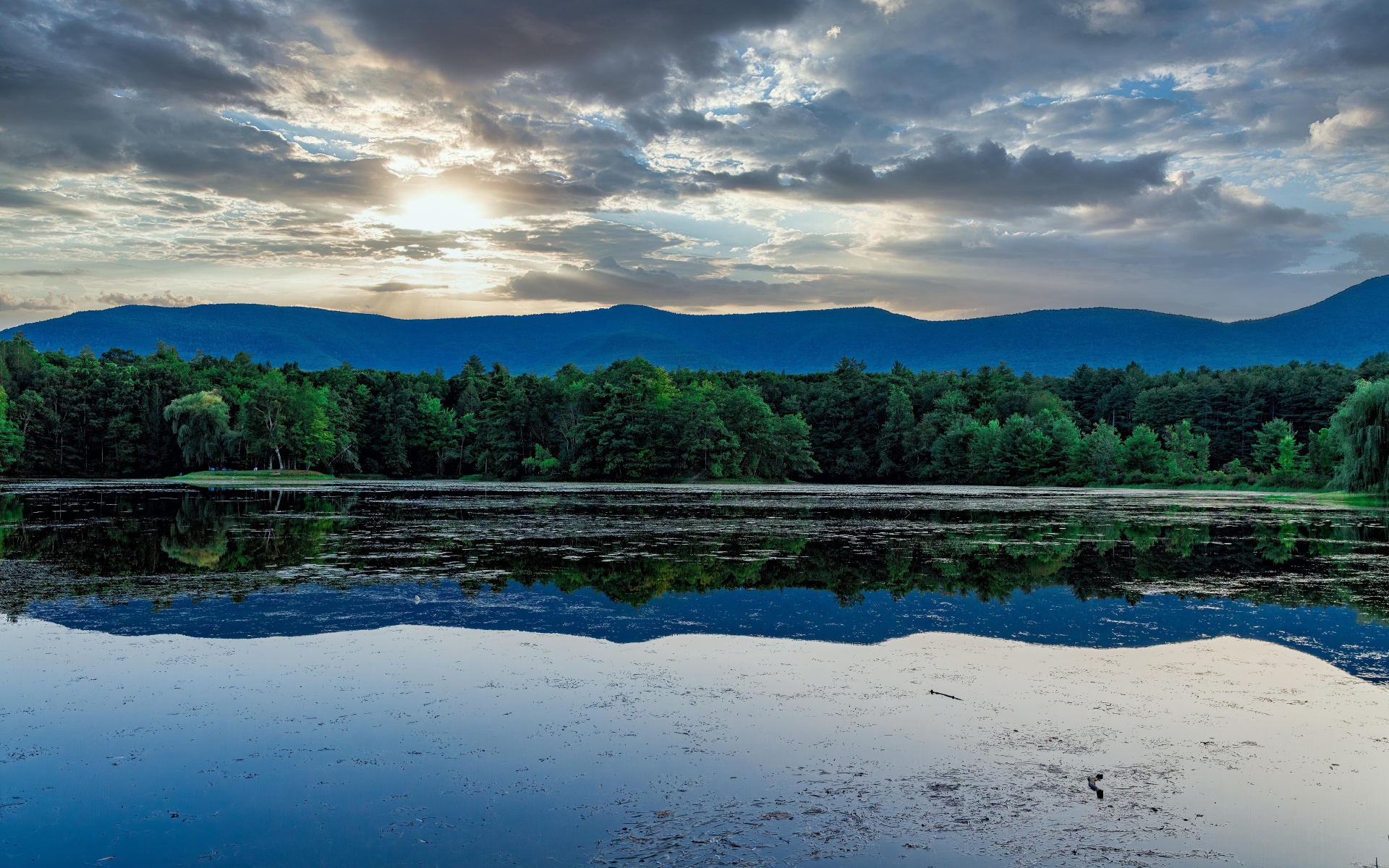 Солнце пробивается сквозь облака в небе над озером