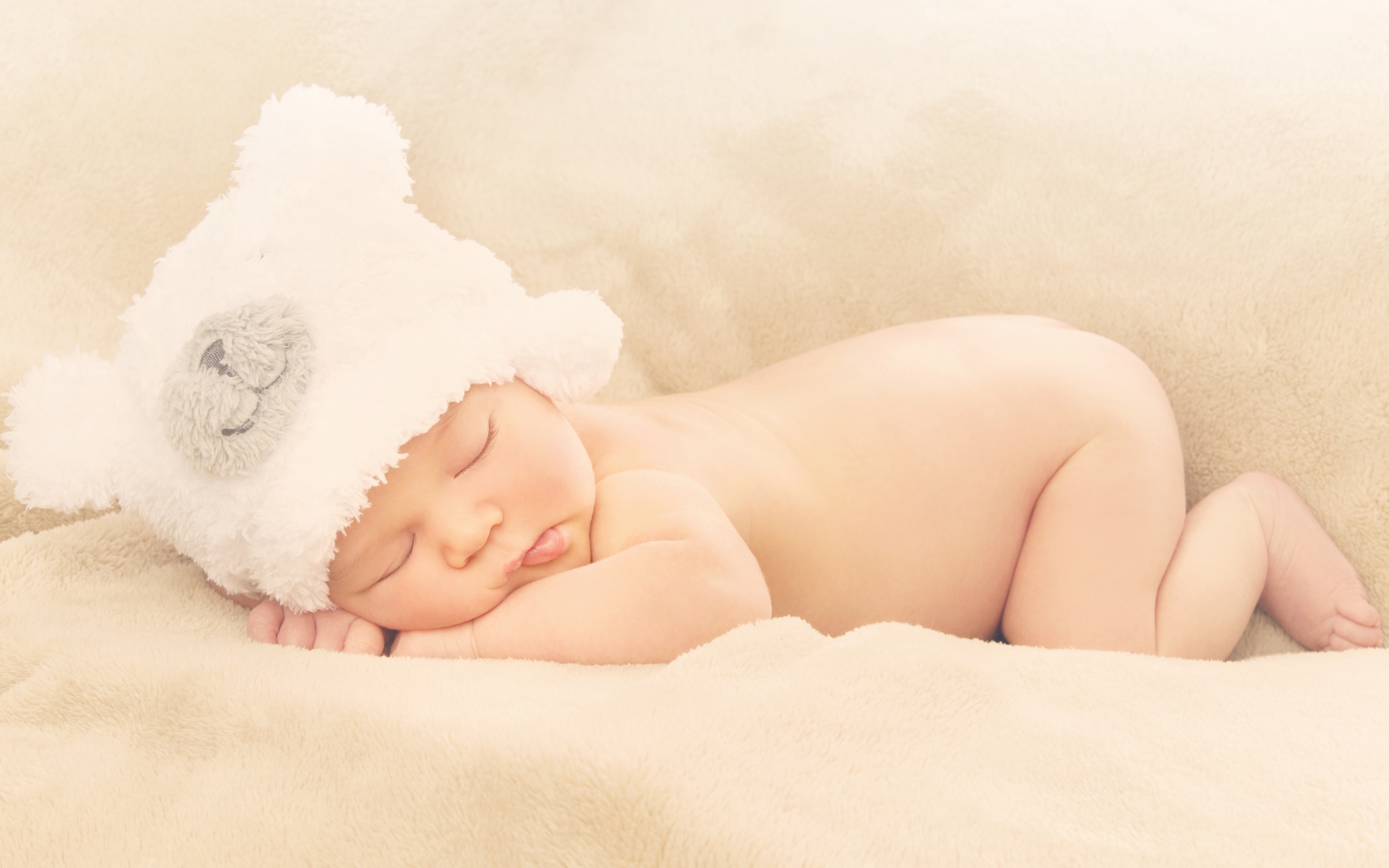 Грудной ребенок с белой шапке спит на кровати