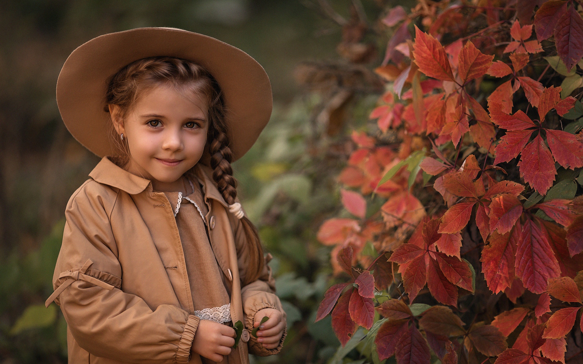 Красивая девочка шляпе стоит у дикого винограда 