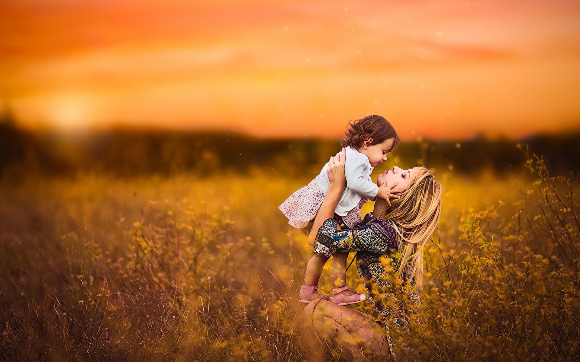 Девушка держит маленькую девочку на руках в поле на закате