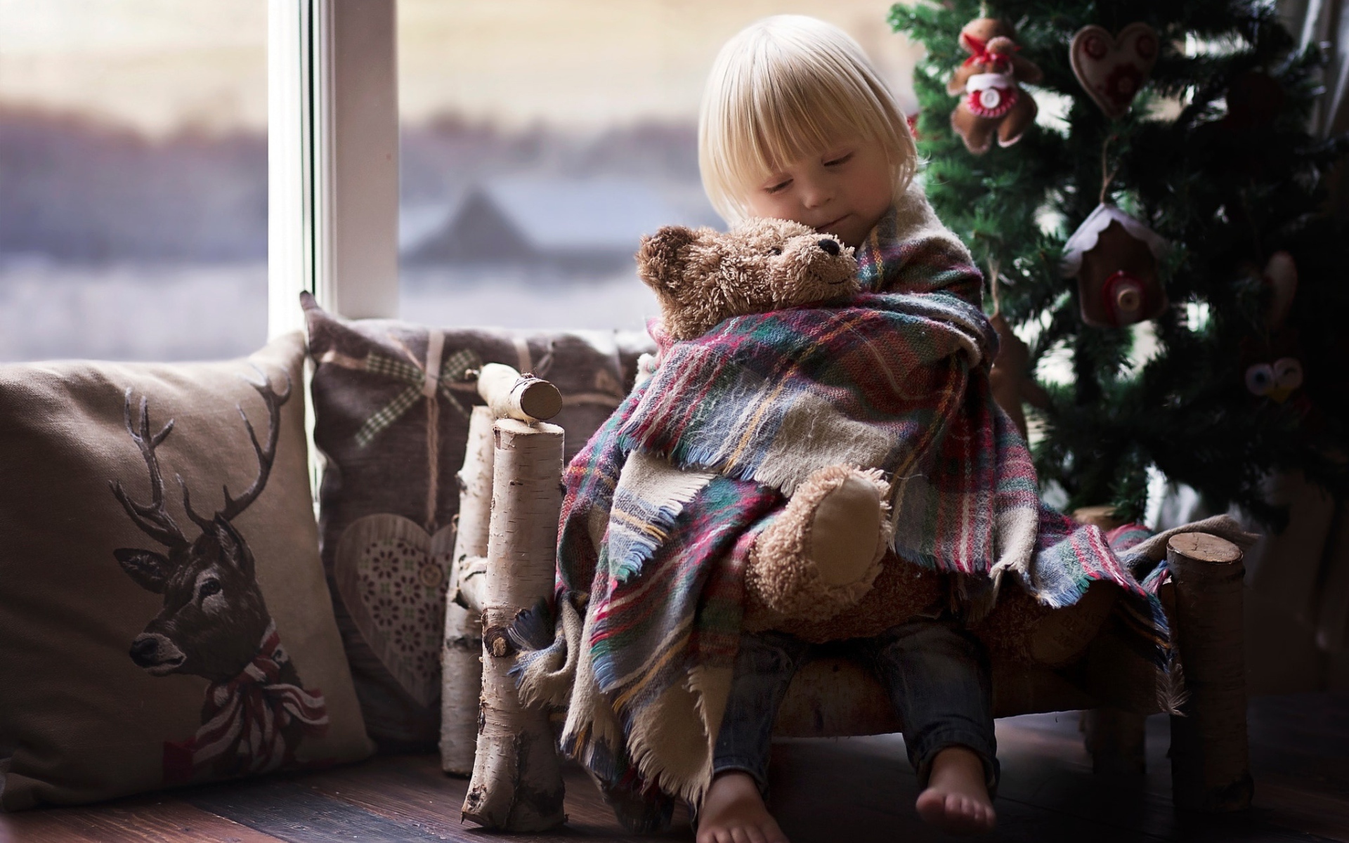 Маленькая девочка обнимает мишку у ели