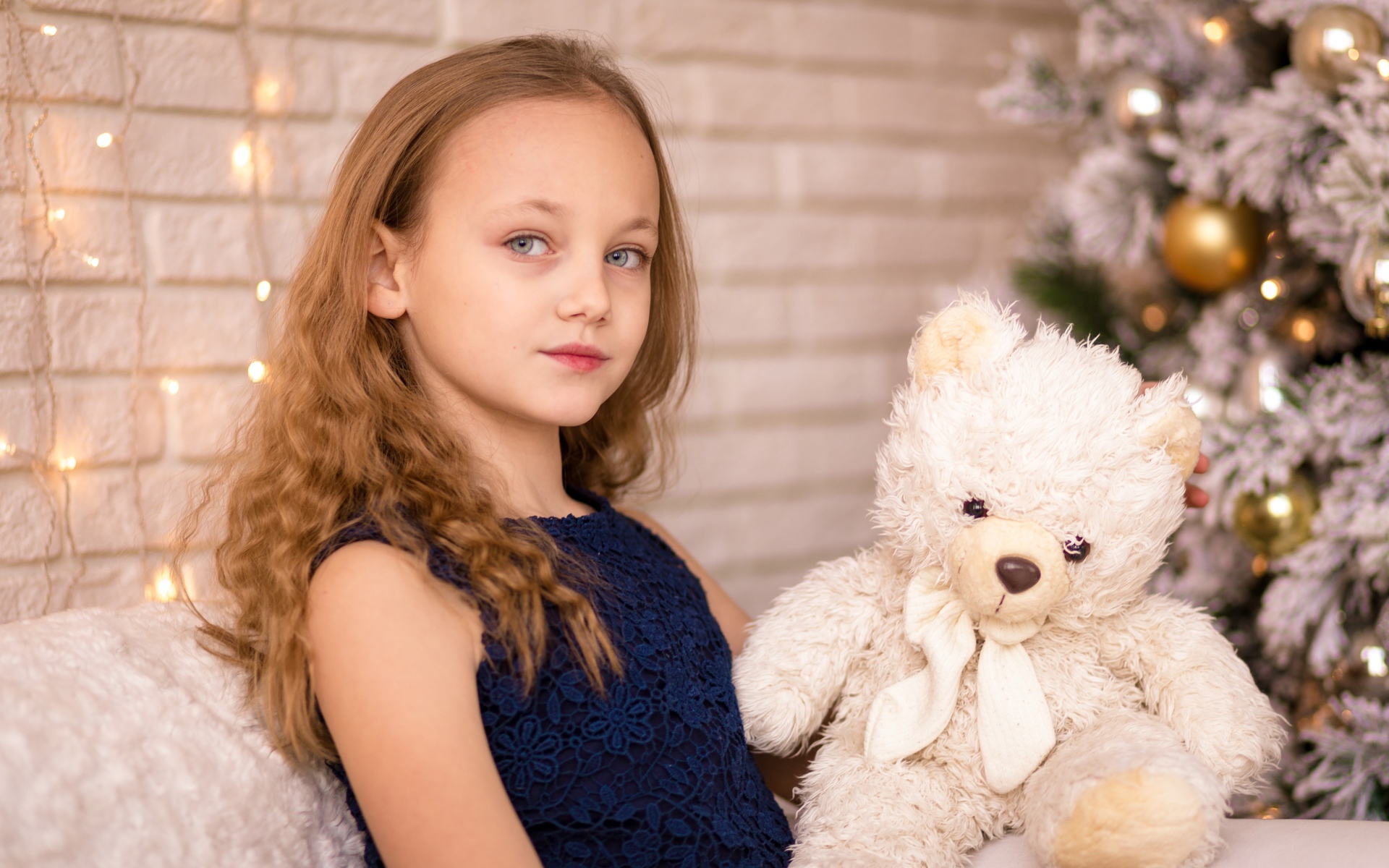 Маленькая девочка с мишкой сидит у наряженной ели 
