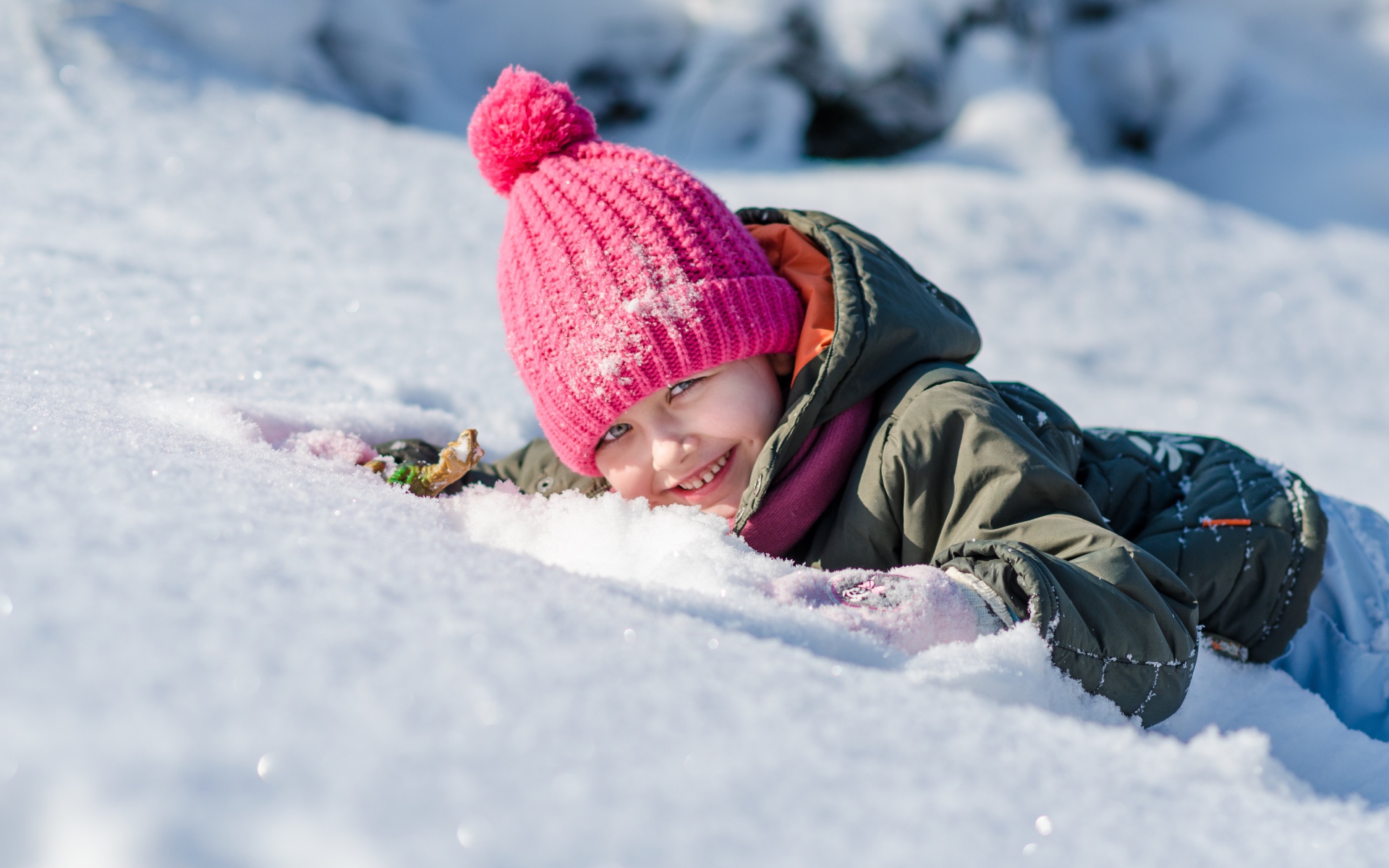 Маленькая улыбающаяся девочка лежит на снегу