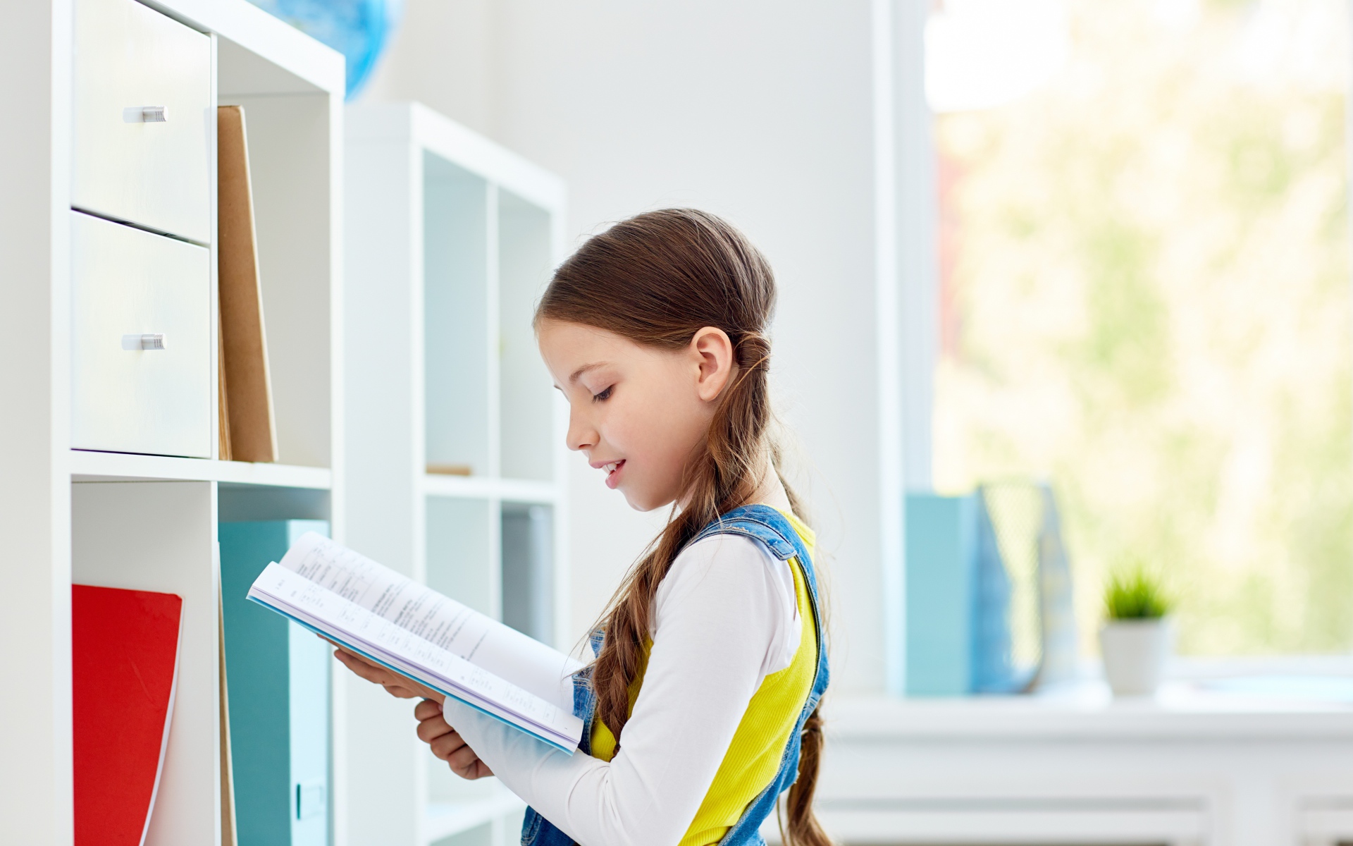 Умная девочка школьница с книгой в библиотеке 