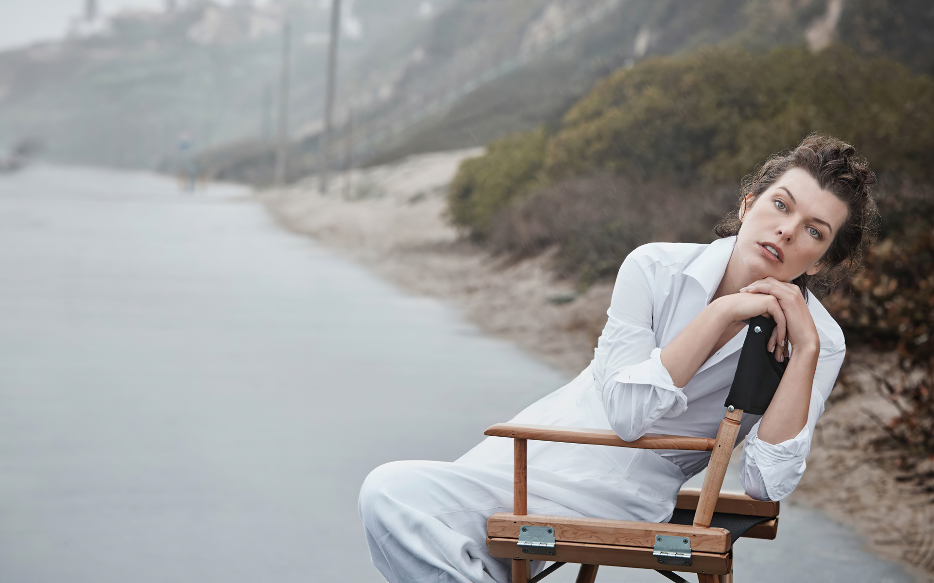 Актриса Милла Йовович в белом платье сидит на стуле