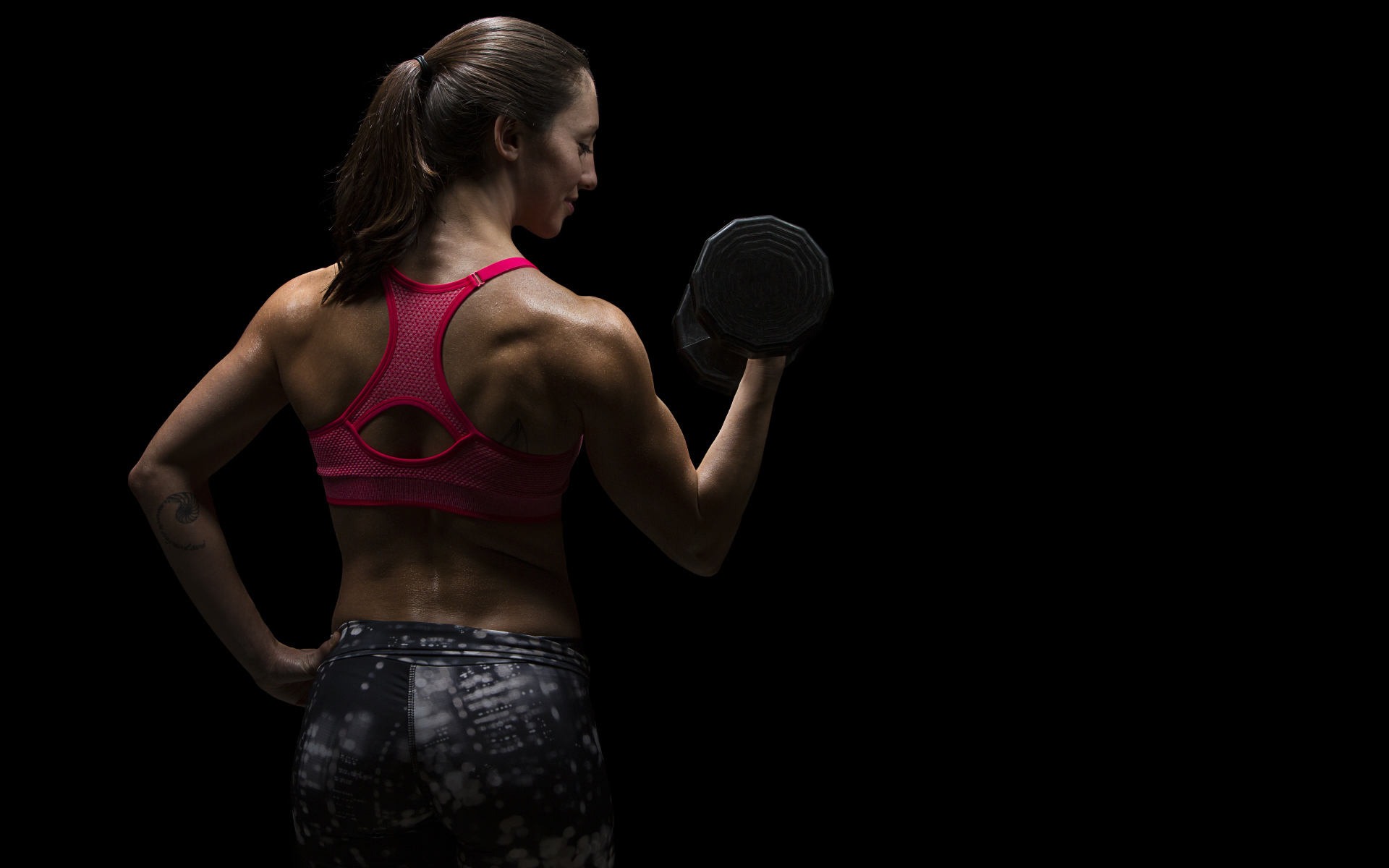 Девушка качает руки гантелей на черном фоне 