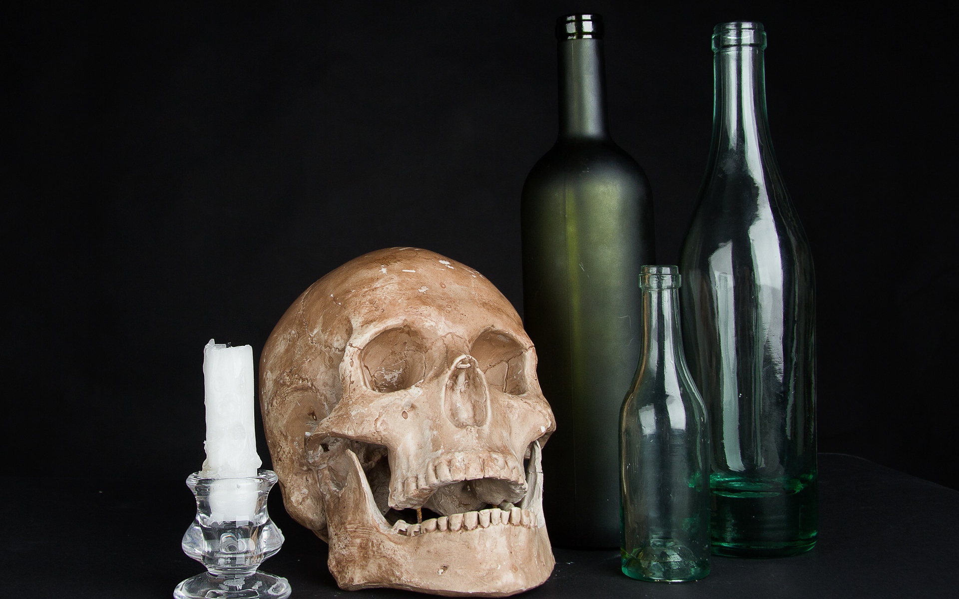 Череп, пустые бутылки и свеча на черном фоне
