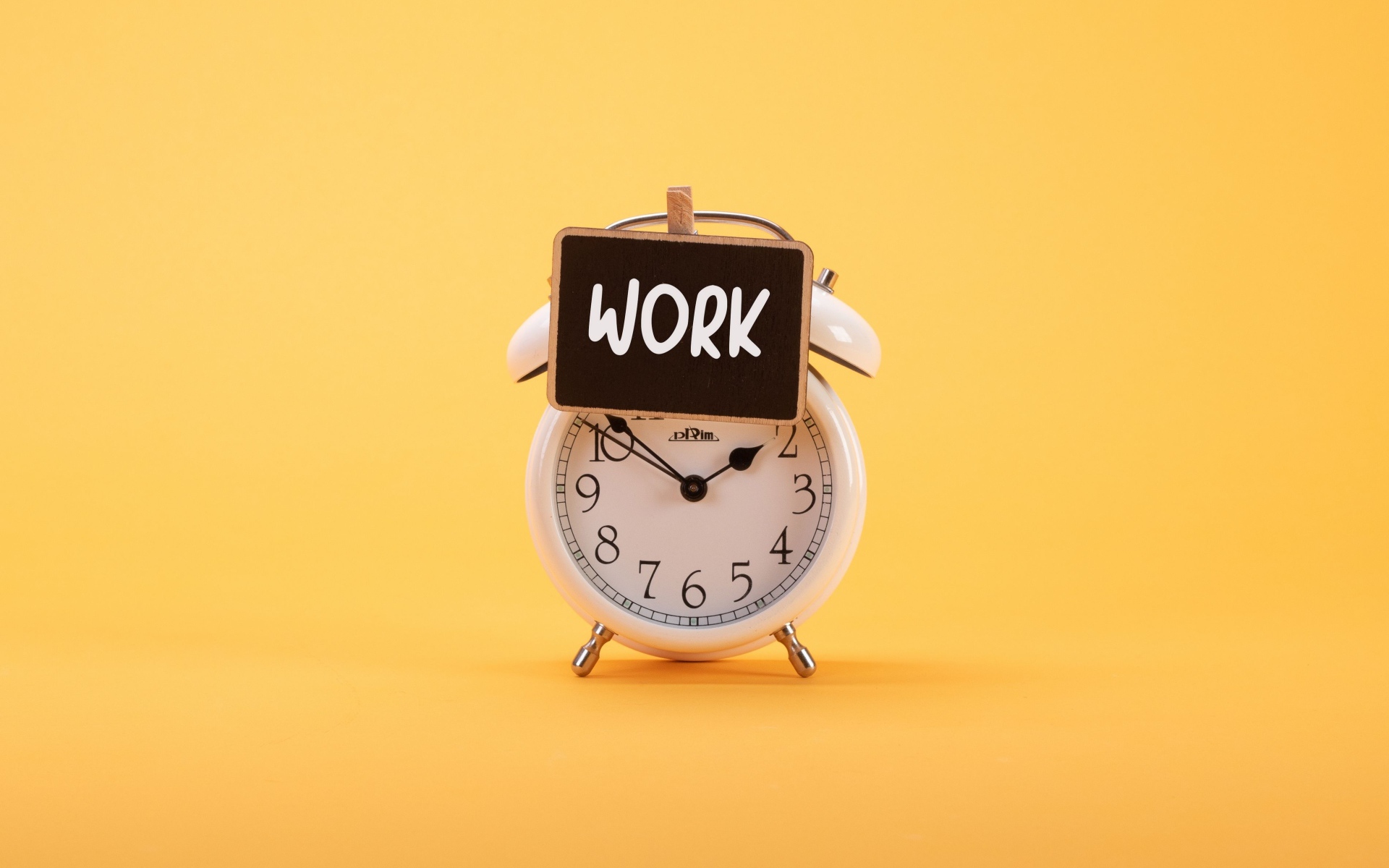 Белый будильник с табличкой на желтом фоне