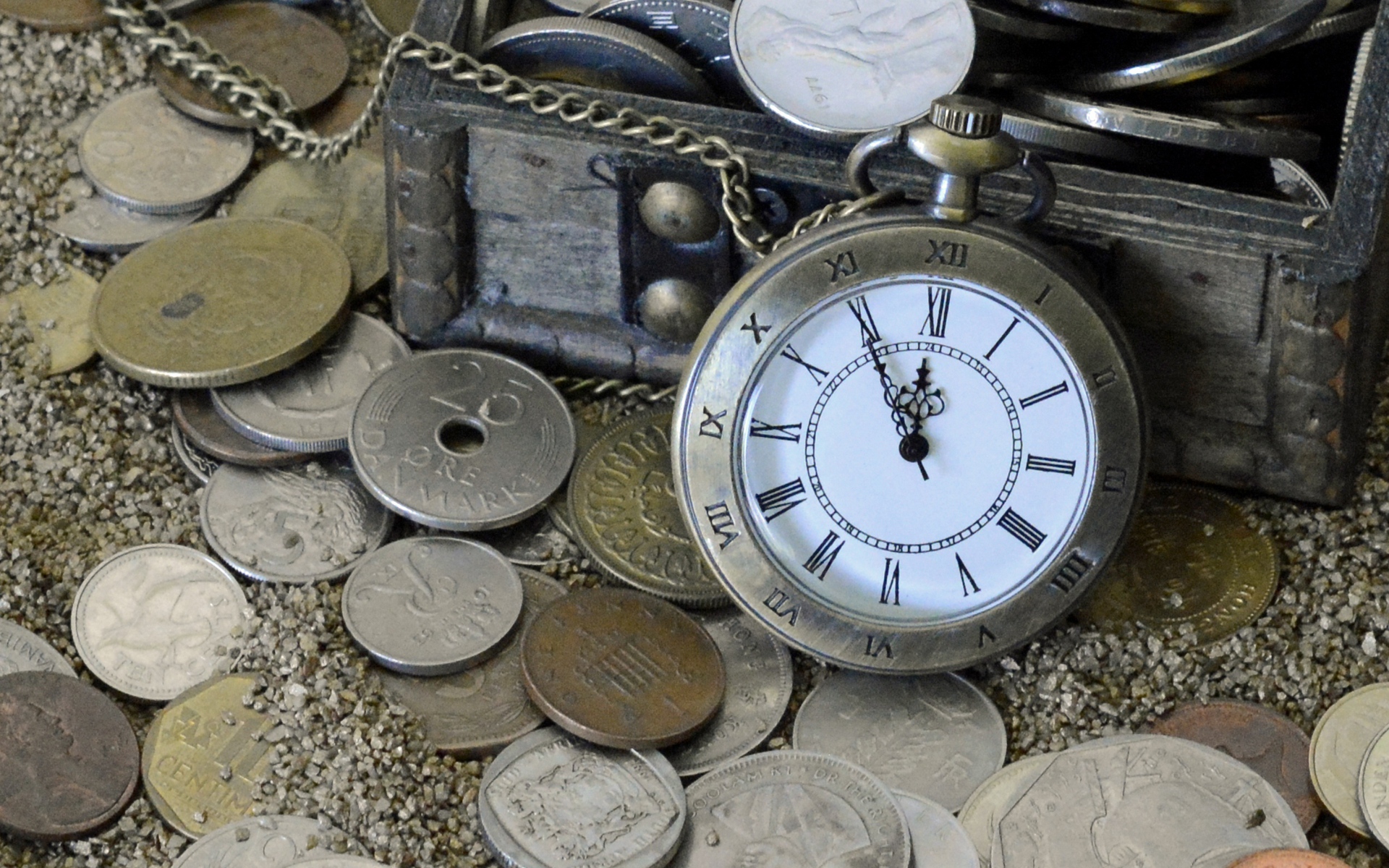Many coins and pocket watch in the sand