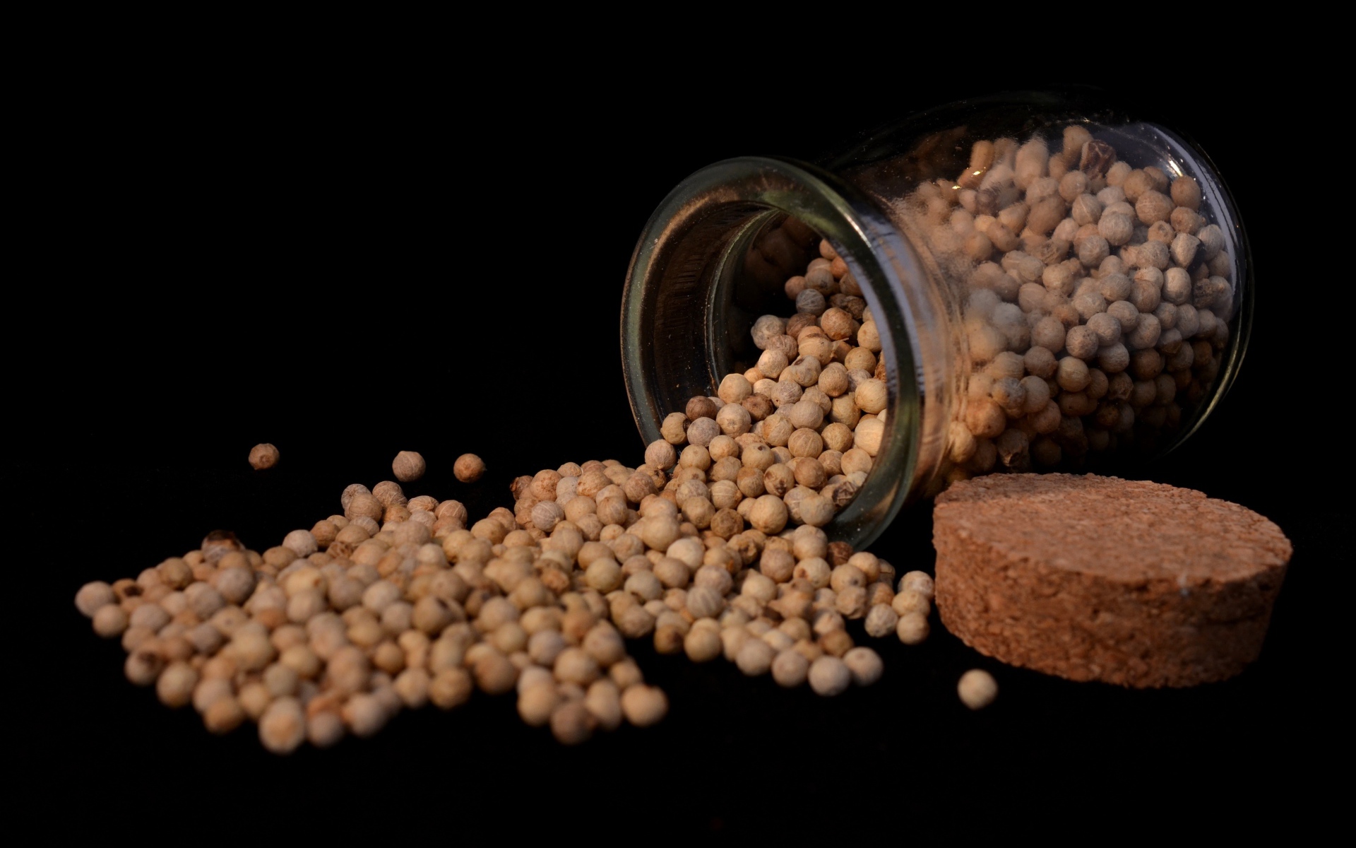 Перец горошек в стеклянной банке на черном фоне 