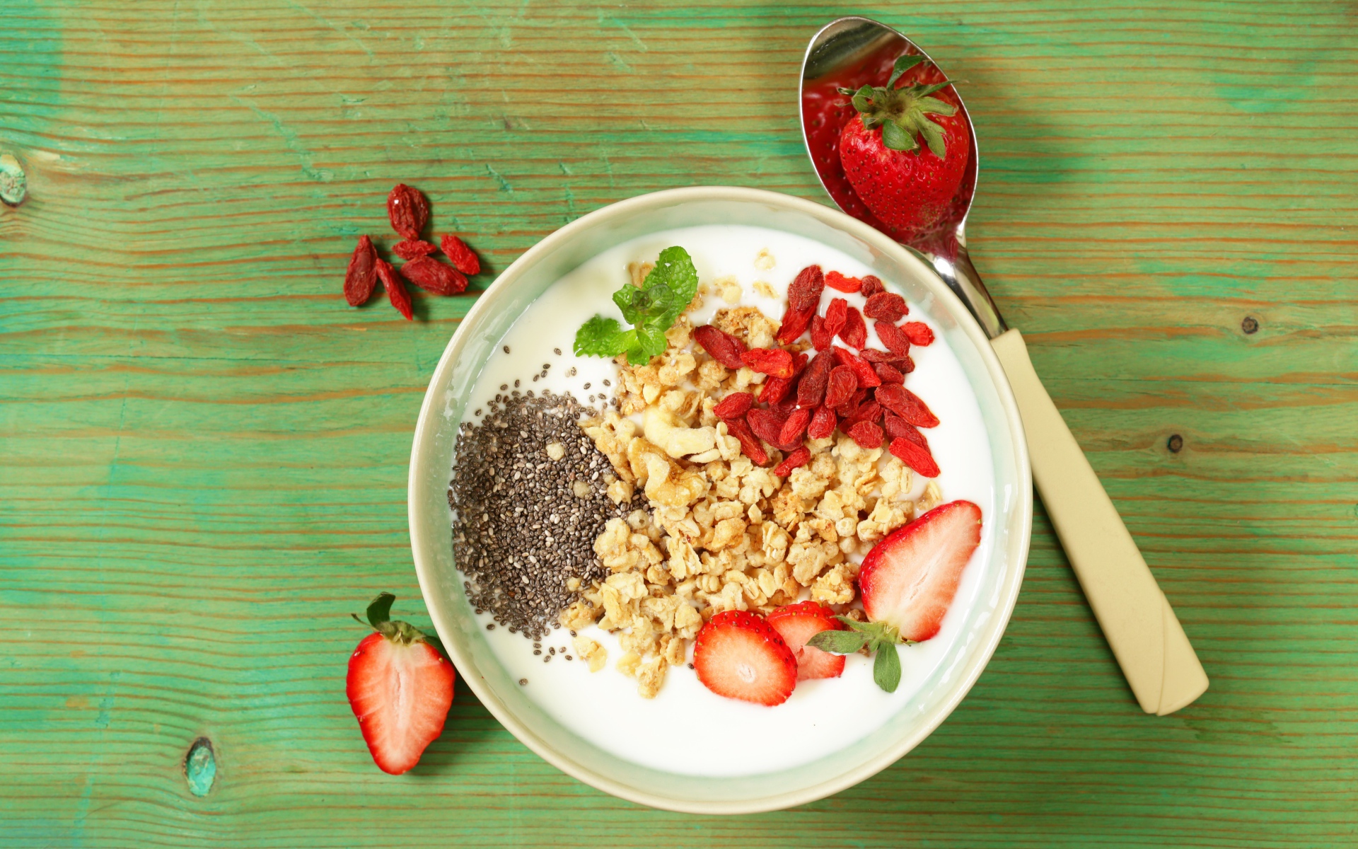 Йогурт с сухофруктами и клубникой на столе в миске 