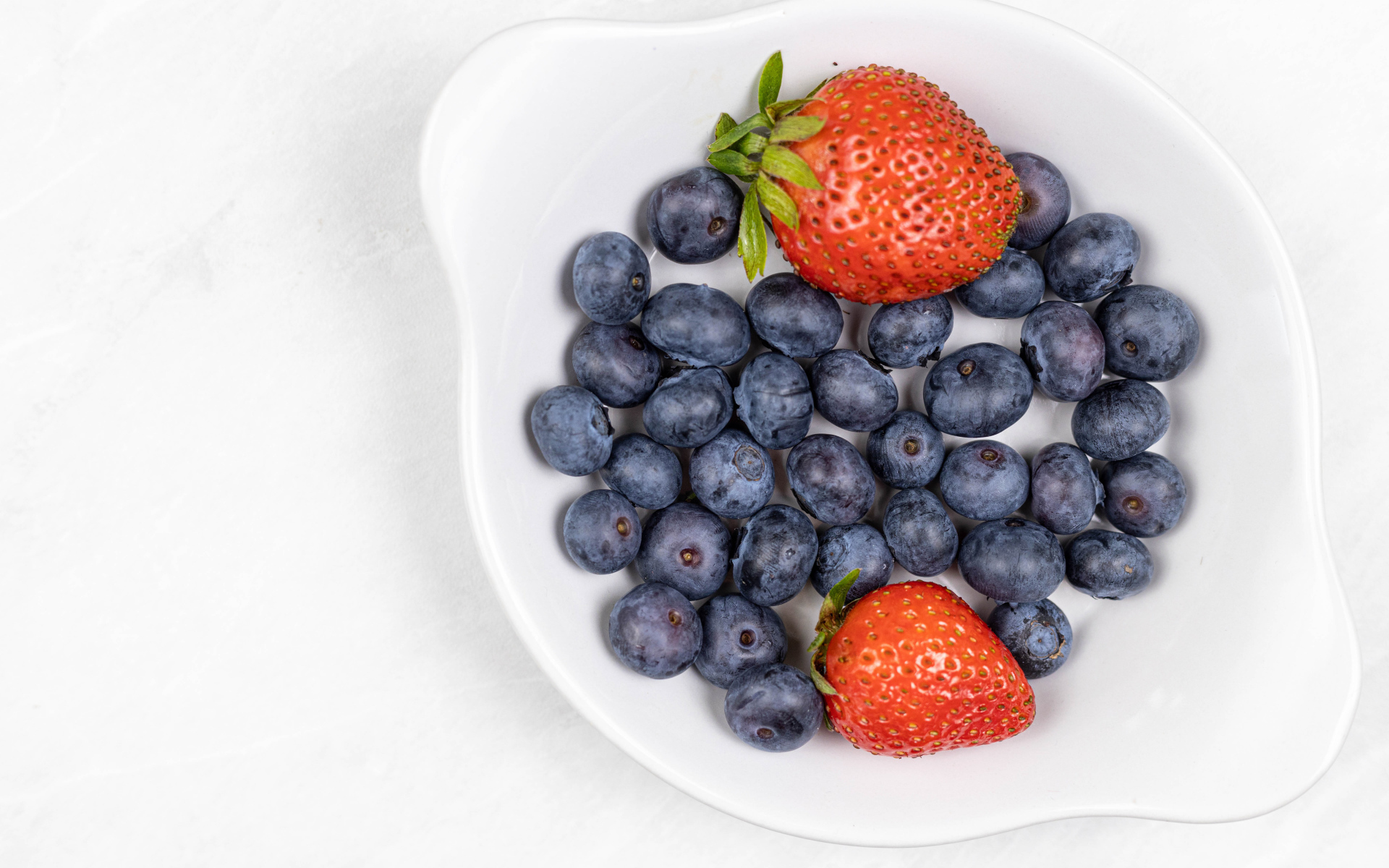 Много синей черники с клубникой в белой тарелке 