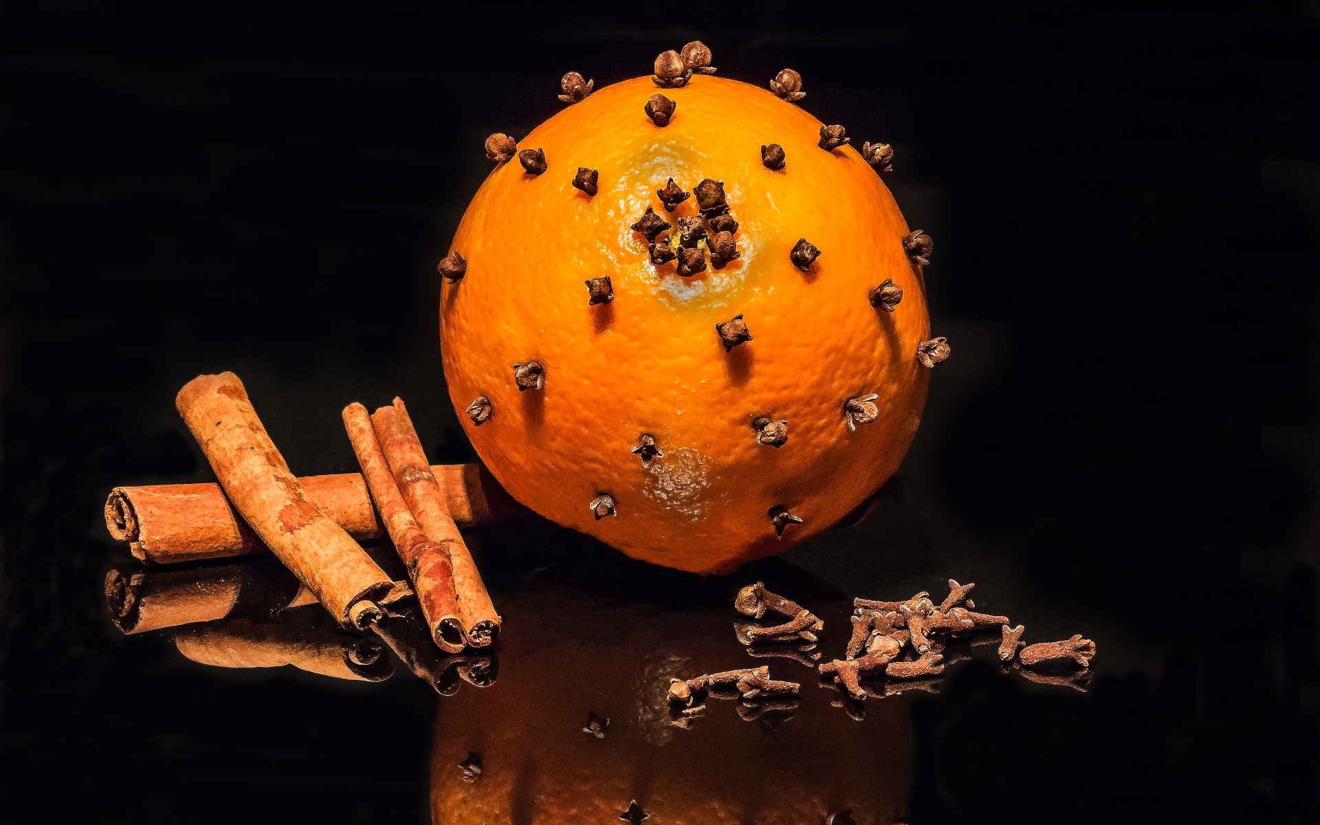 Оранжевый апельсин с гвоздикой и корицей на черном фоне 
