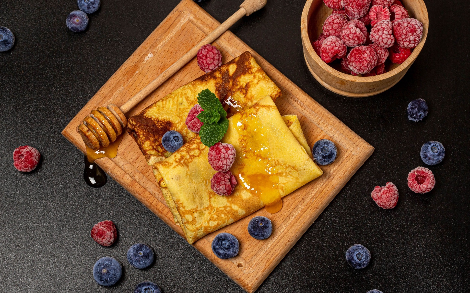 Pancakes with honey and blueberries and raspberries on a black table