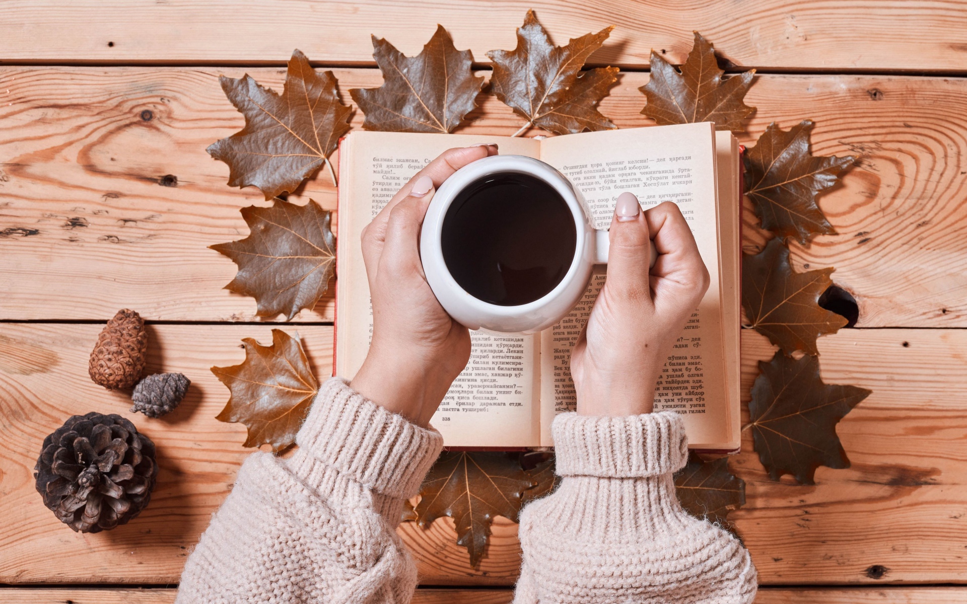 Чашка кофе в руках на столе с книгой и листьями