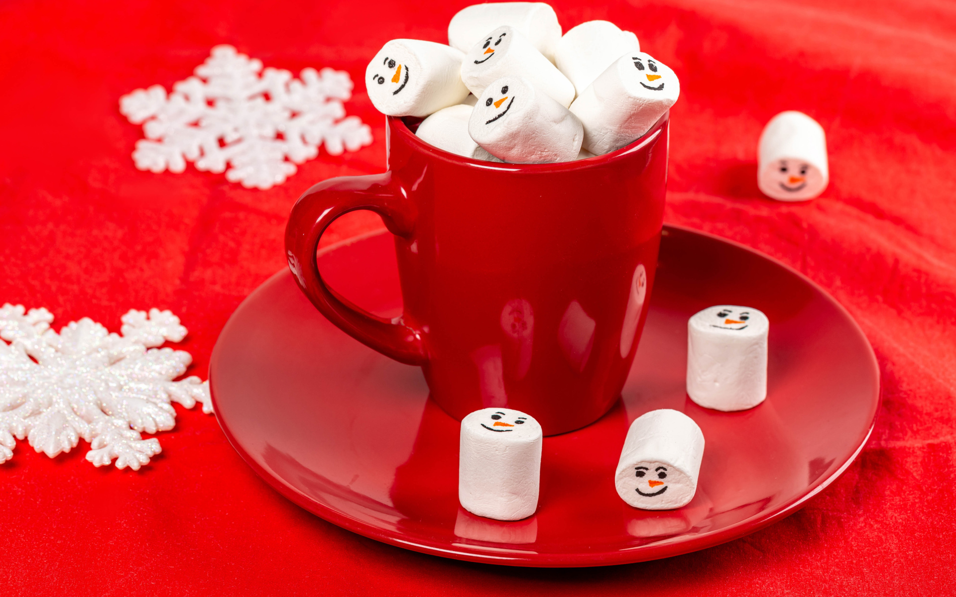 Красная чашка с маршмеллоу на столе со снежинками