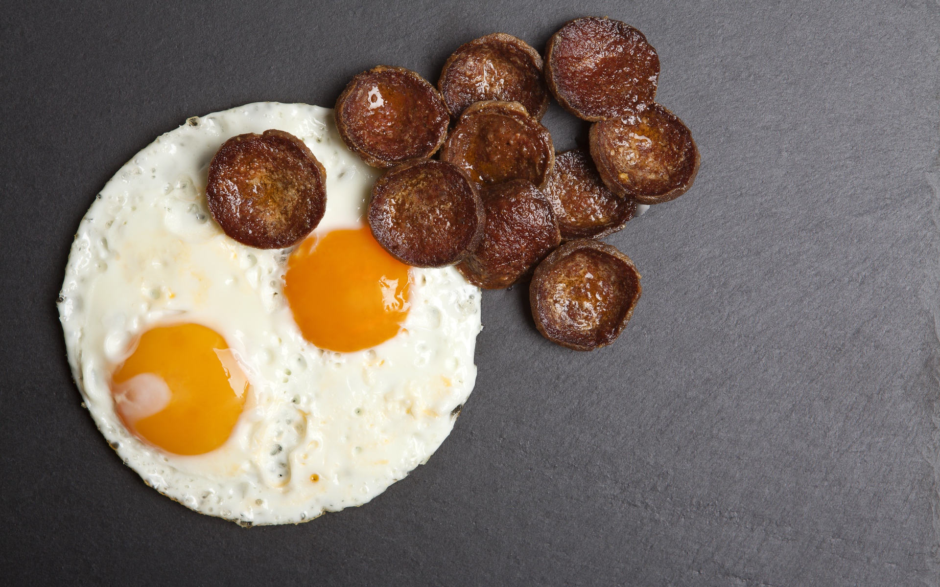 Жареная колбаса с яичницей глазуньей на сером столе 