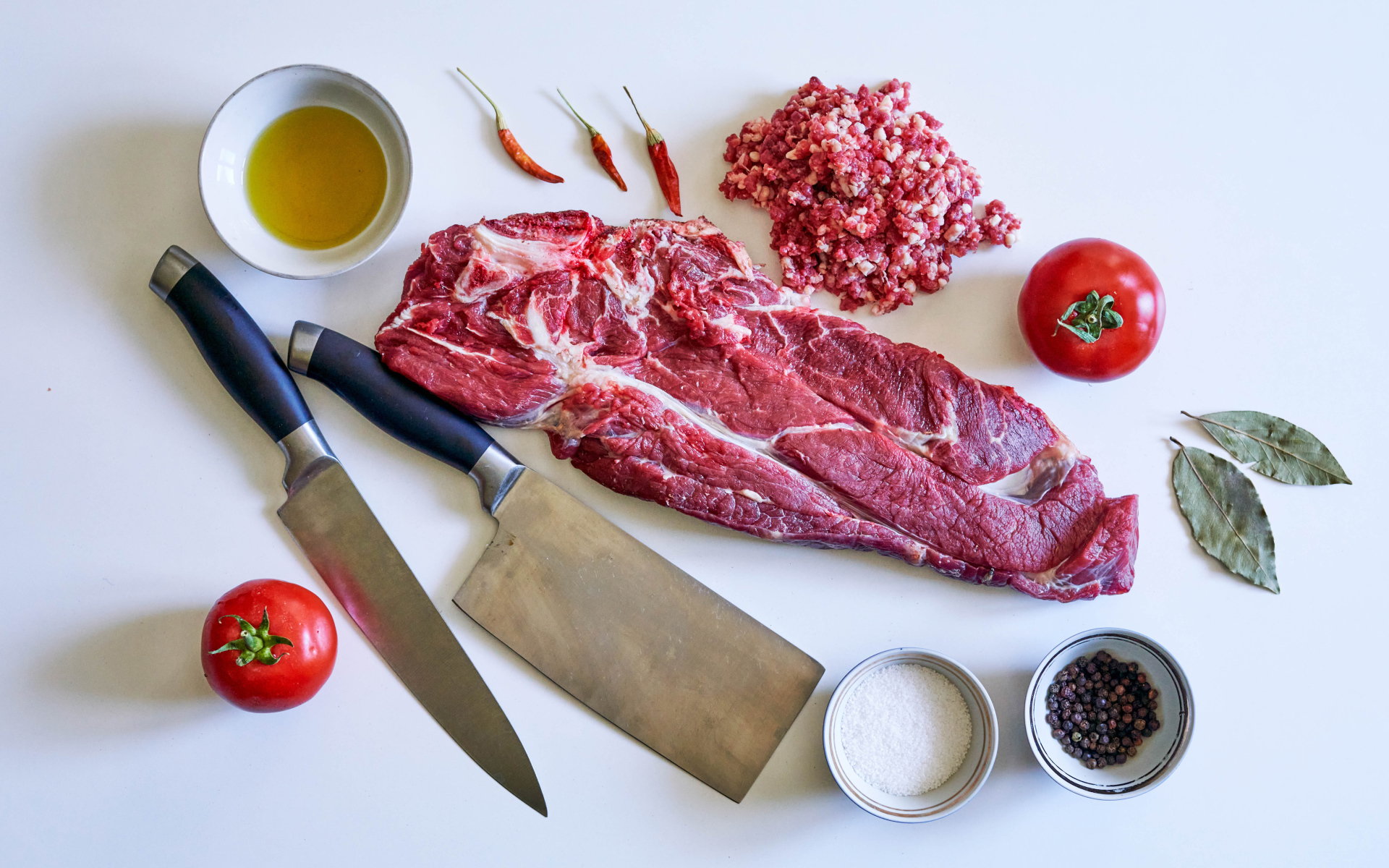 Кусок мяса со специями и ножами на столе 