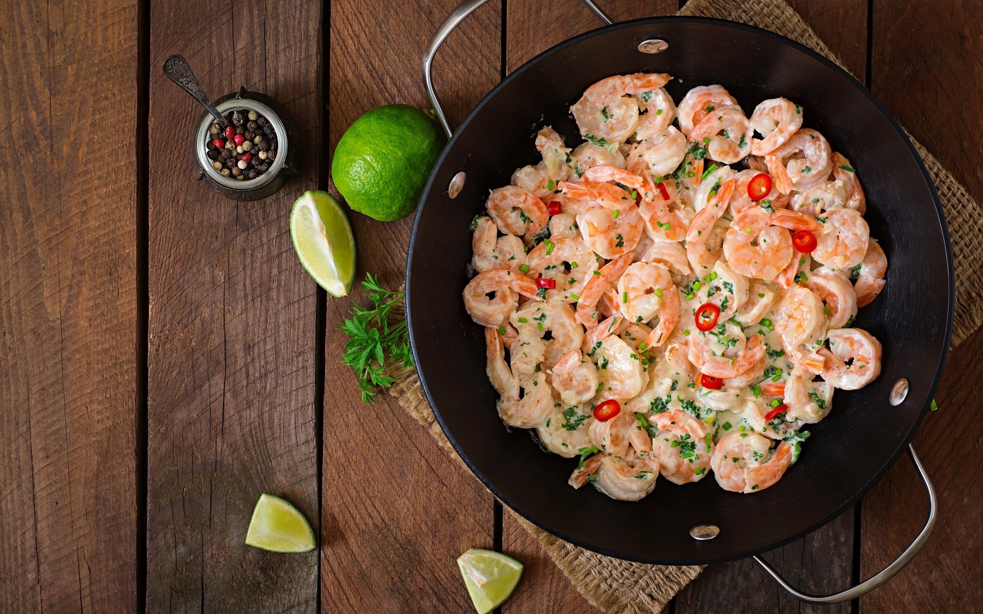 Креветки с соусом в сковороде на столе с лаймом