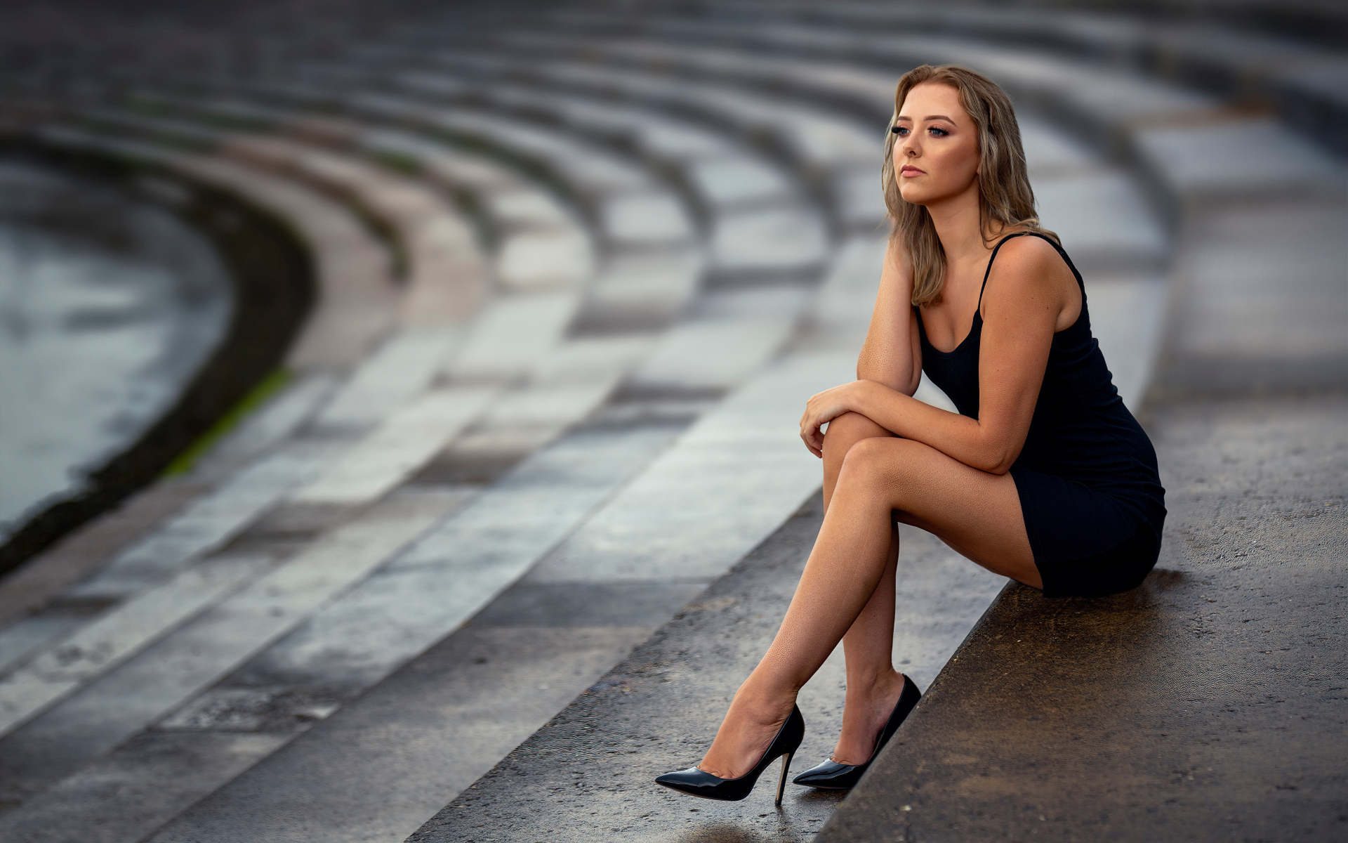 Девушка в коротком черном платье сидит на ступеньках