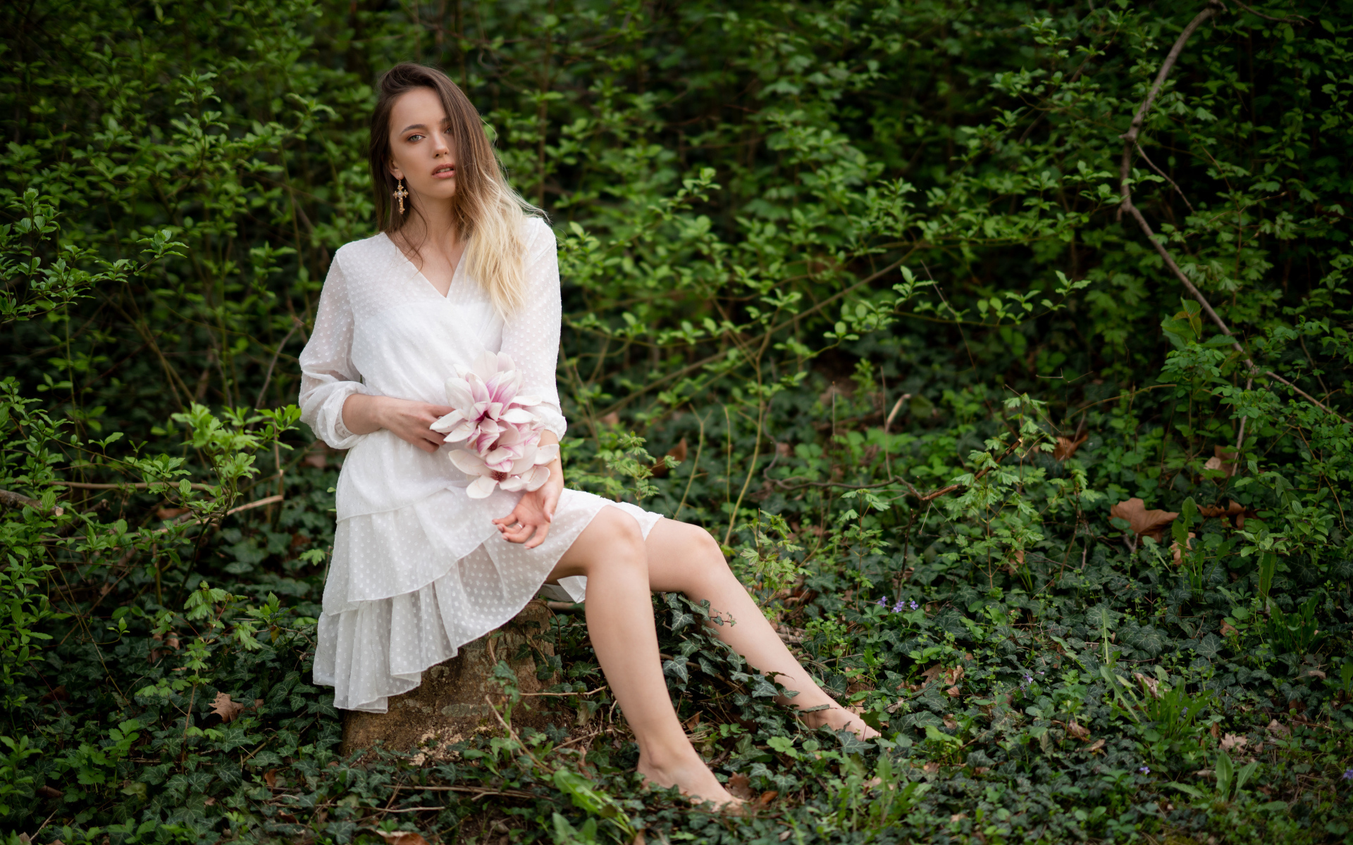 Молодая девушка в белом платье сидит на камне в лесу 