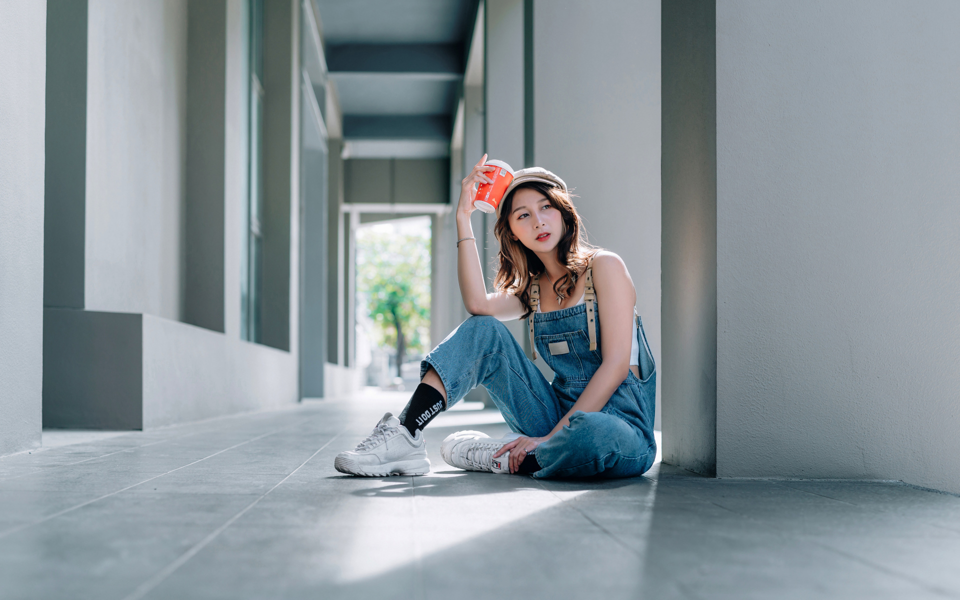 Девушка азиатка в синем комбинезоне с кофе в руке 