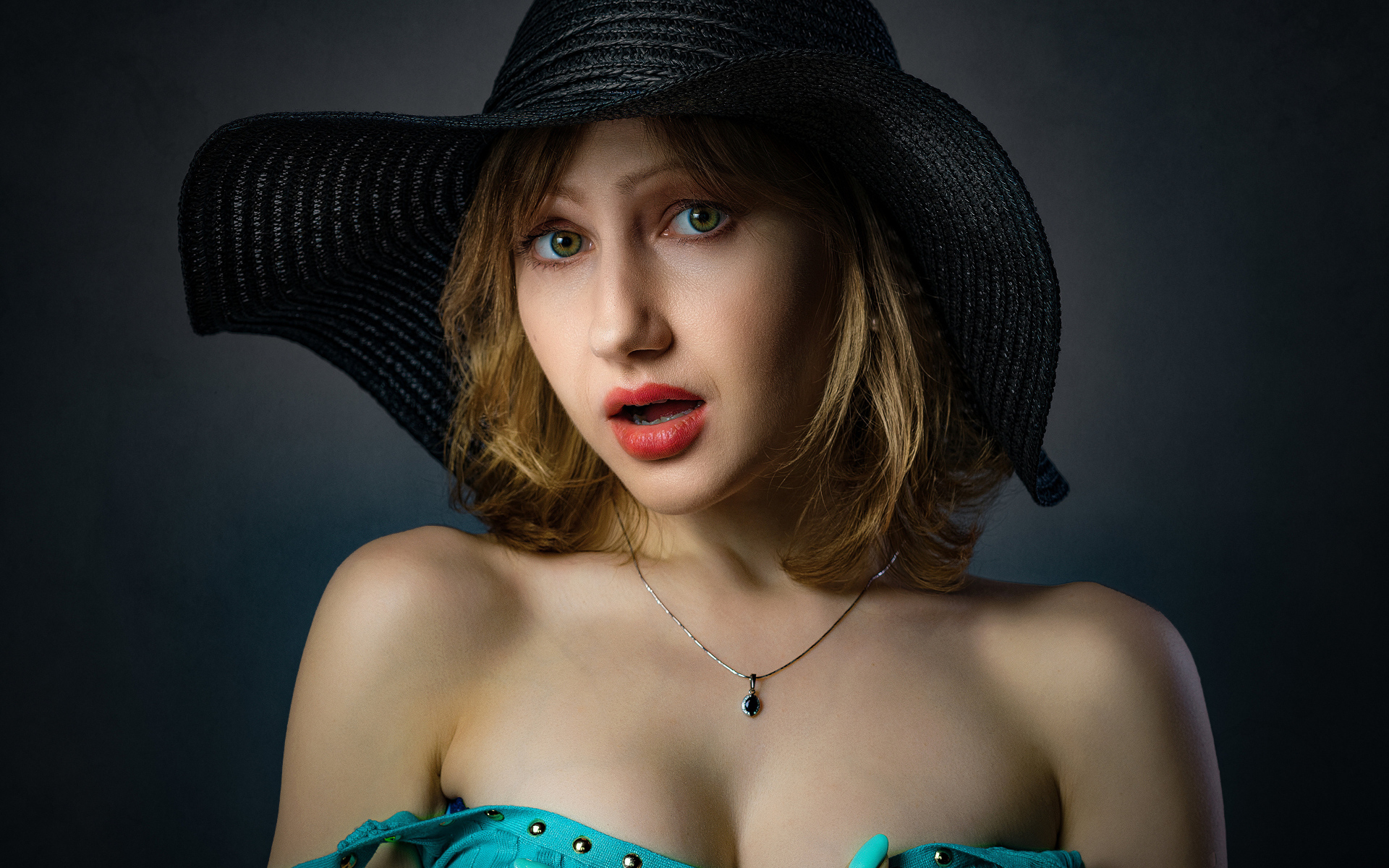 Красивая девушка в большой черной шляпе на сером фоне 