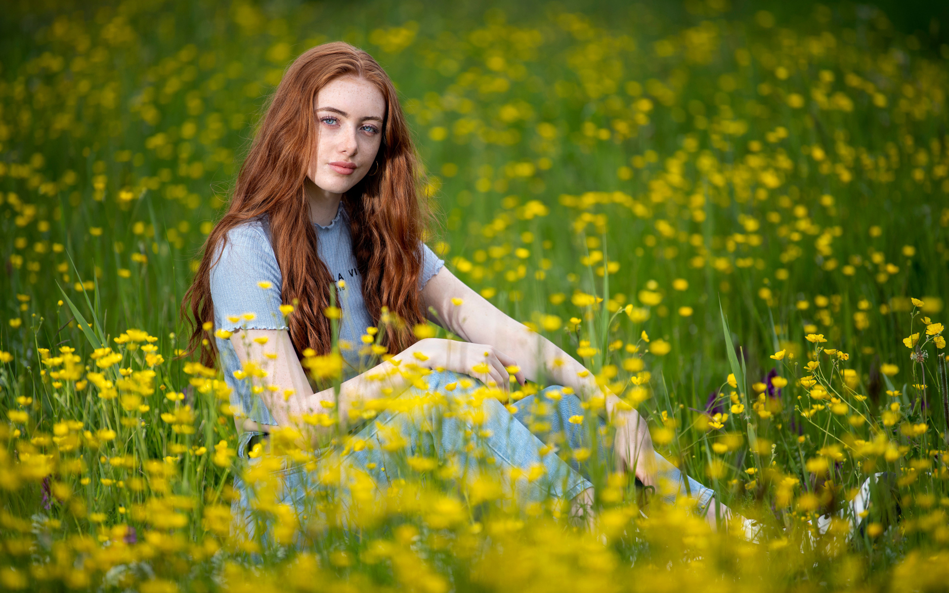 Голубоглазая девушка сидит на поле с желтыми цветами
