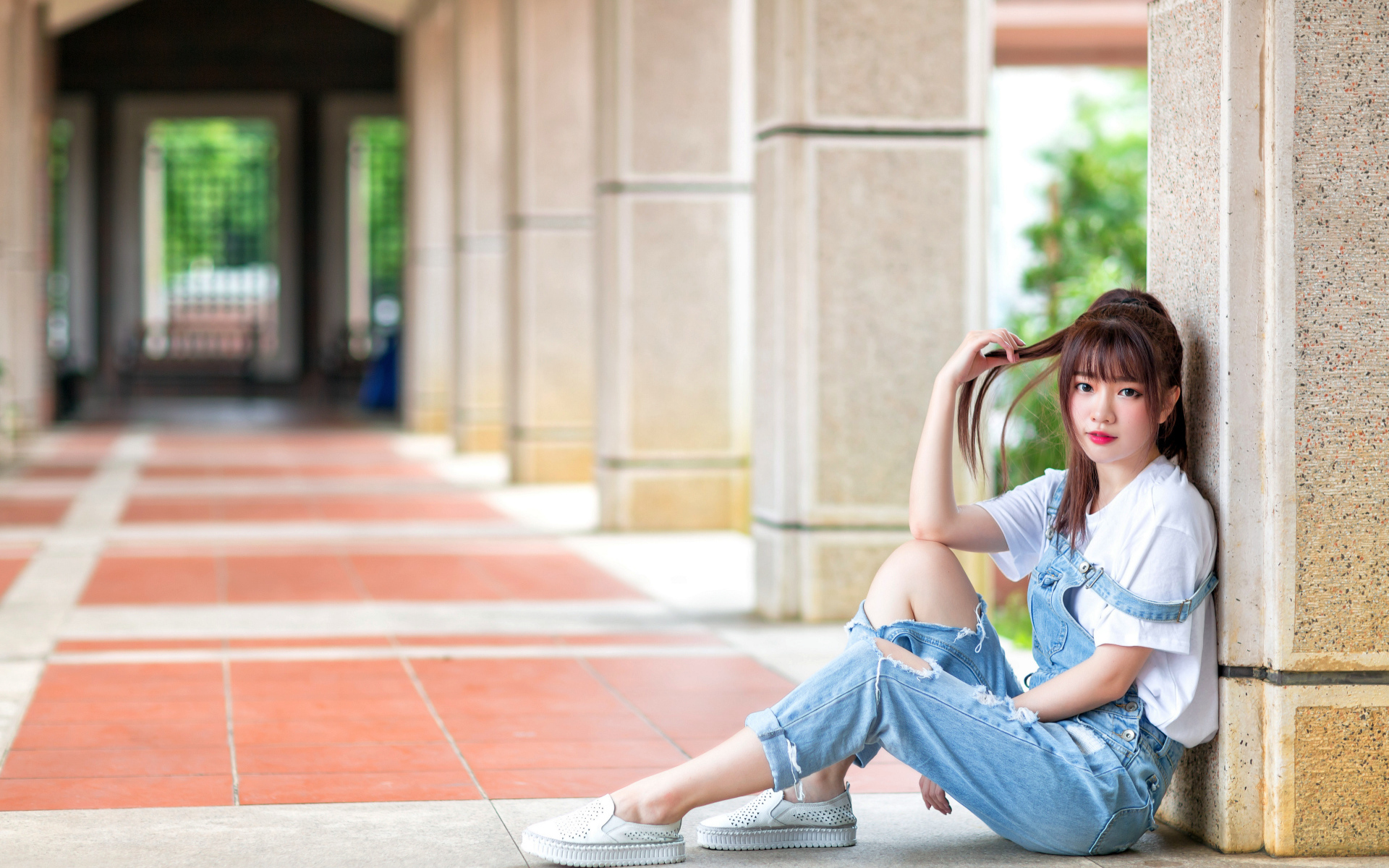 Грустная девушка азиатка сидит у колонны