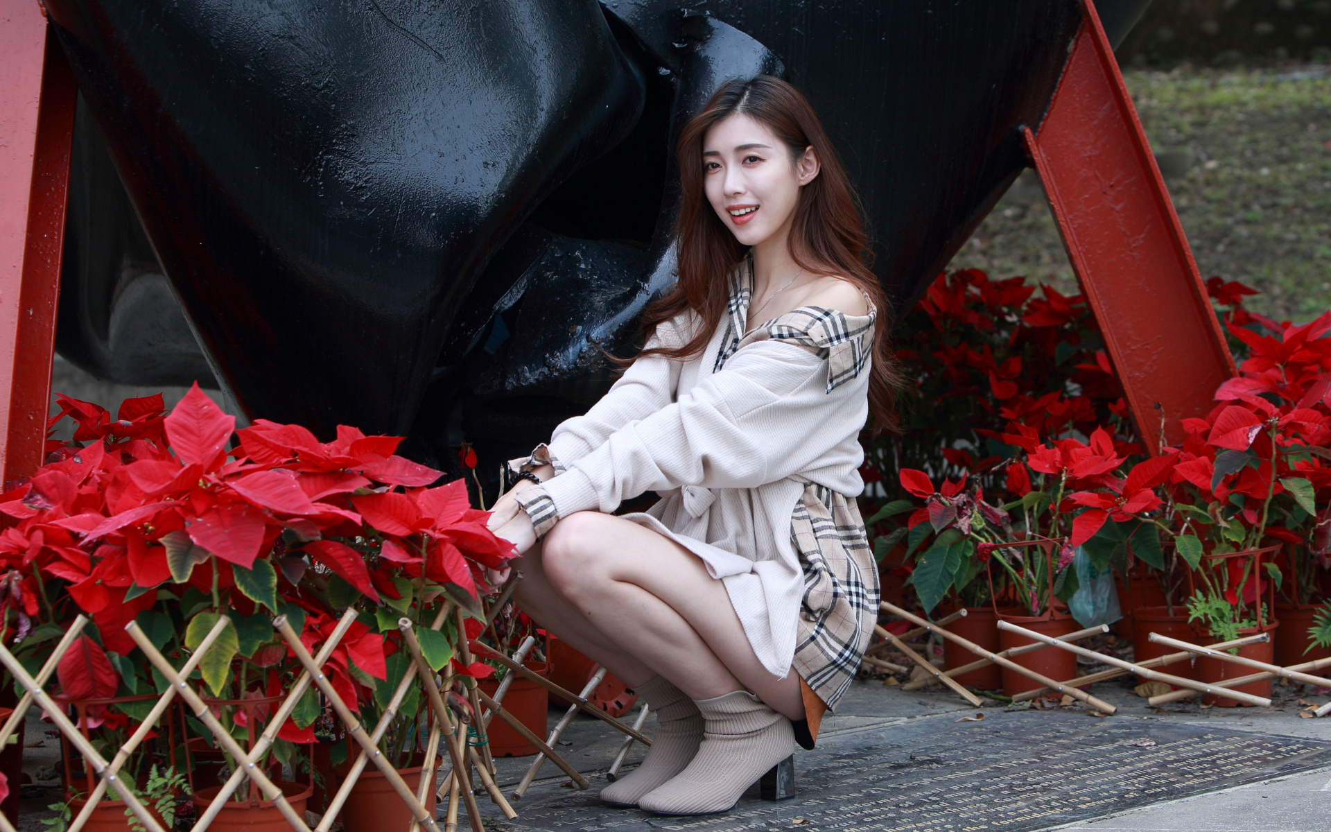 Улыбающаяся азиатка сидит у красных цветов 