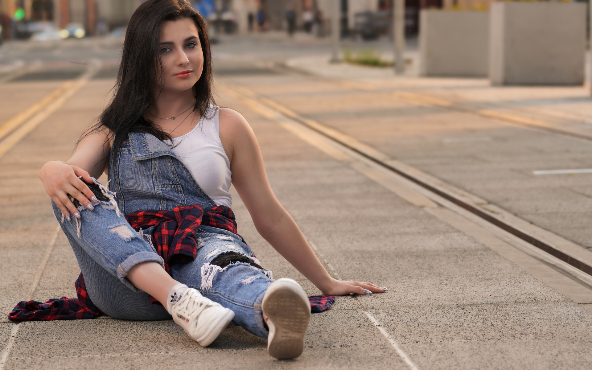 Молодая девушка в джинсовом наряде сидит на асфальте