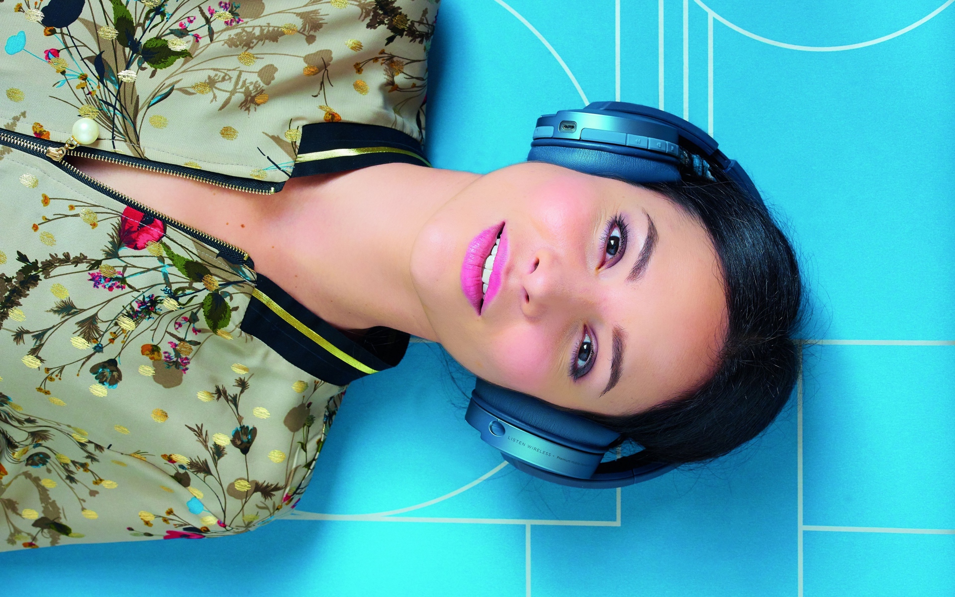 Молодая женщина в наушниках лежит на голубом полу