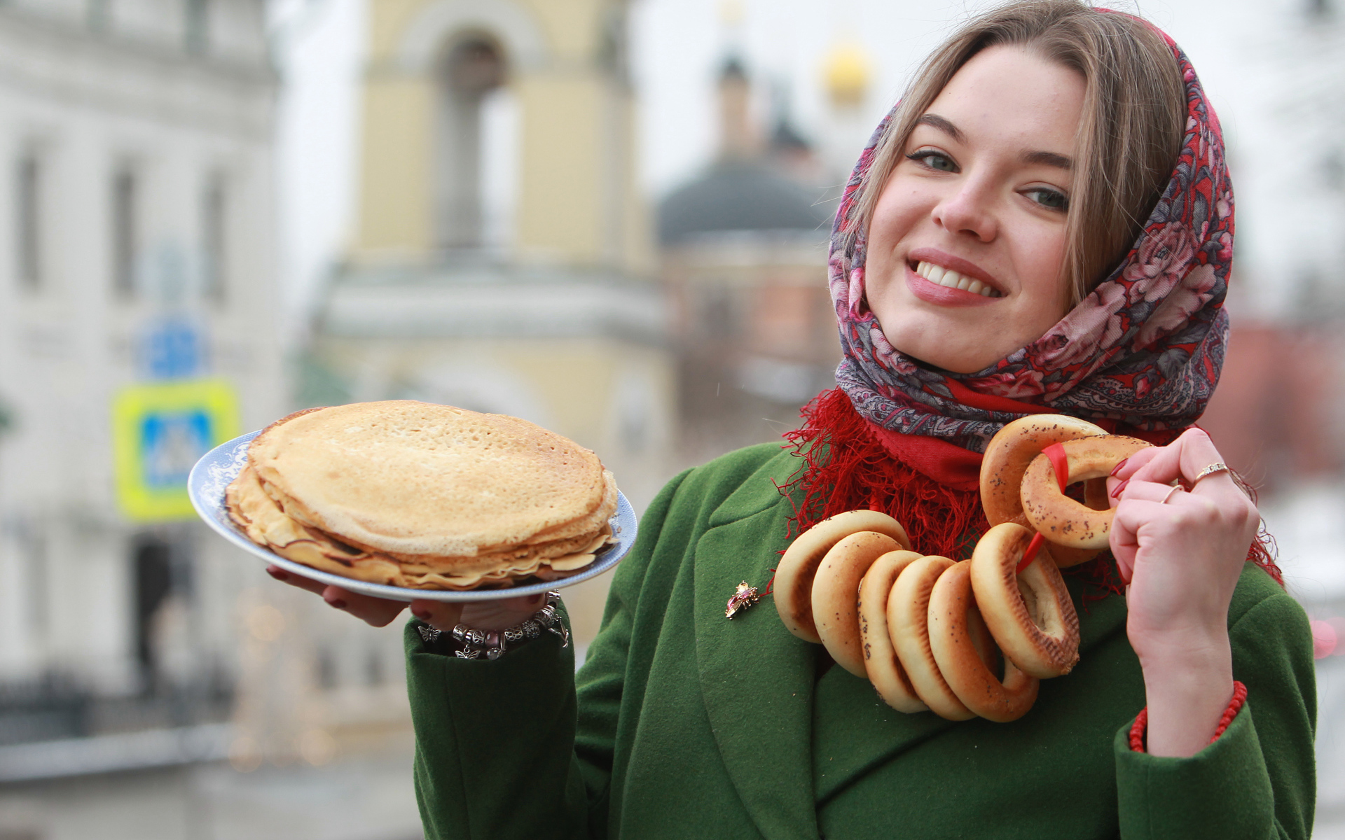 Улыбающаяся девушка с блинами и баранками на Масленицу
