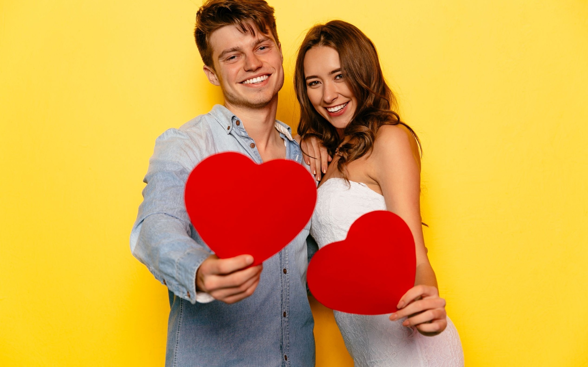 Влюбленная пара на желтом фоне с бумажными сердечками в руках 