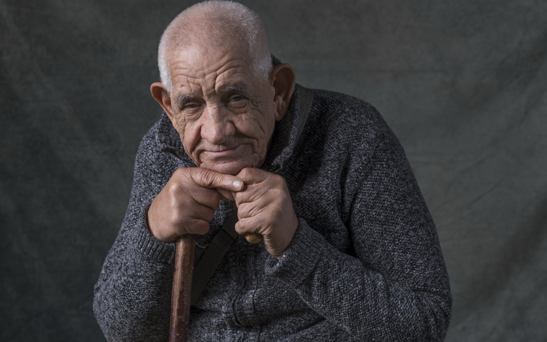 Пожилой мужчина в теплом свитере на сером фоне 