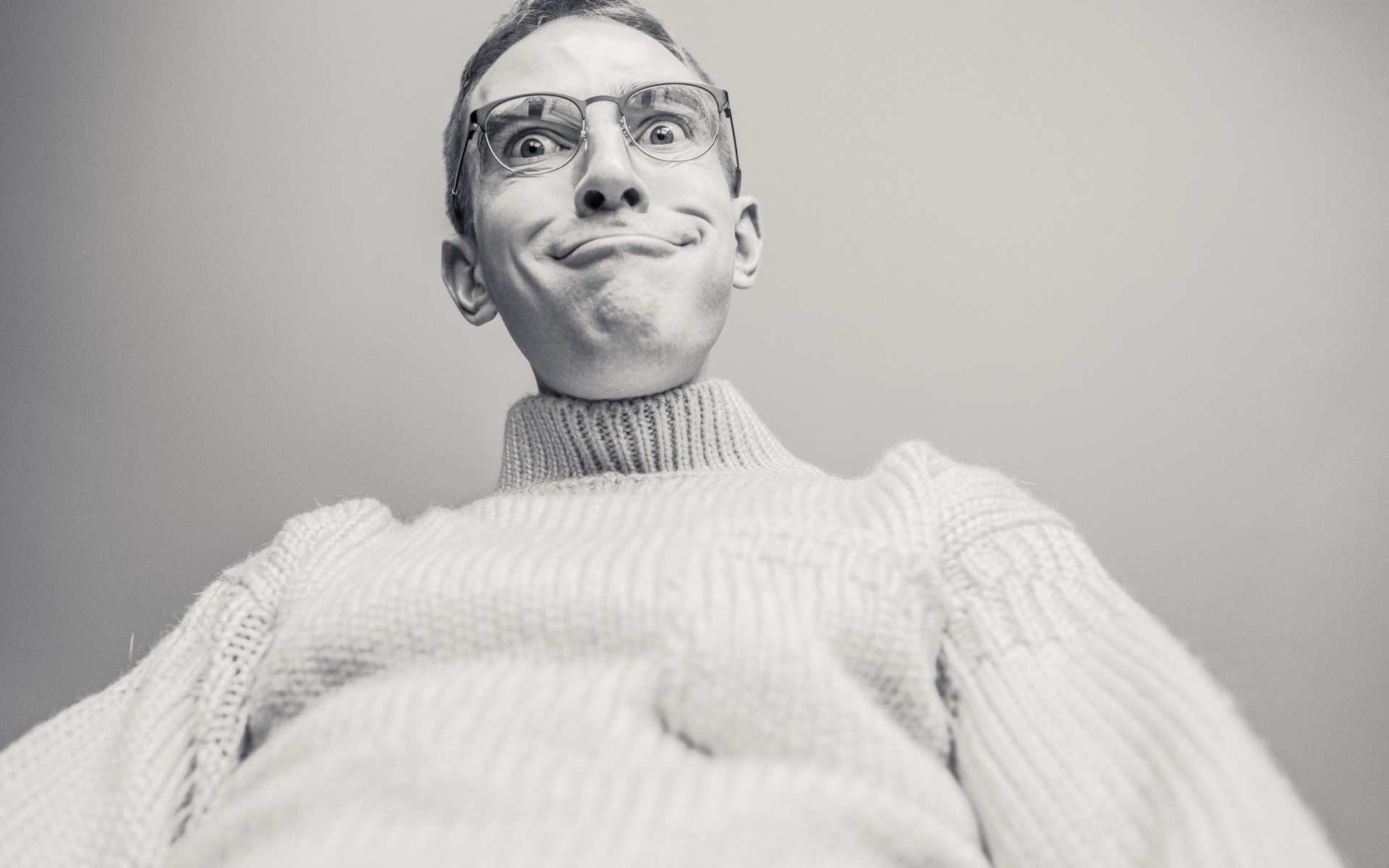 Мужчина в очках корчит лицо на сером фоне