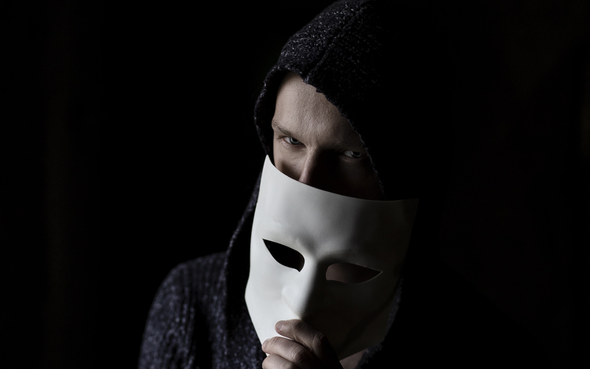 A man covers his face with a white mask on a black background